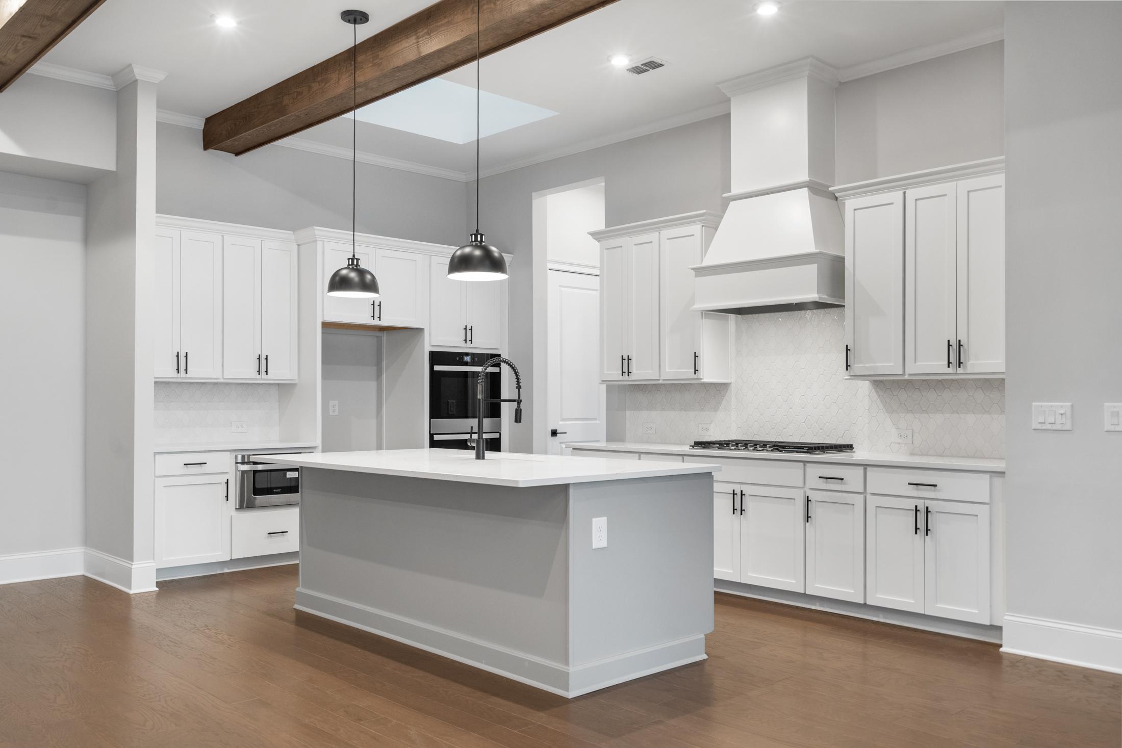 Gourmet kitchen in The Seaside by Davidson Homes featuring white shaker cabinets, gray quartz island, stainless appliances, and wood beam ceiling