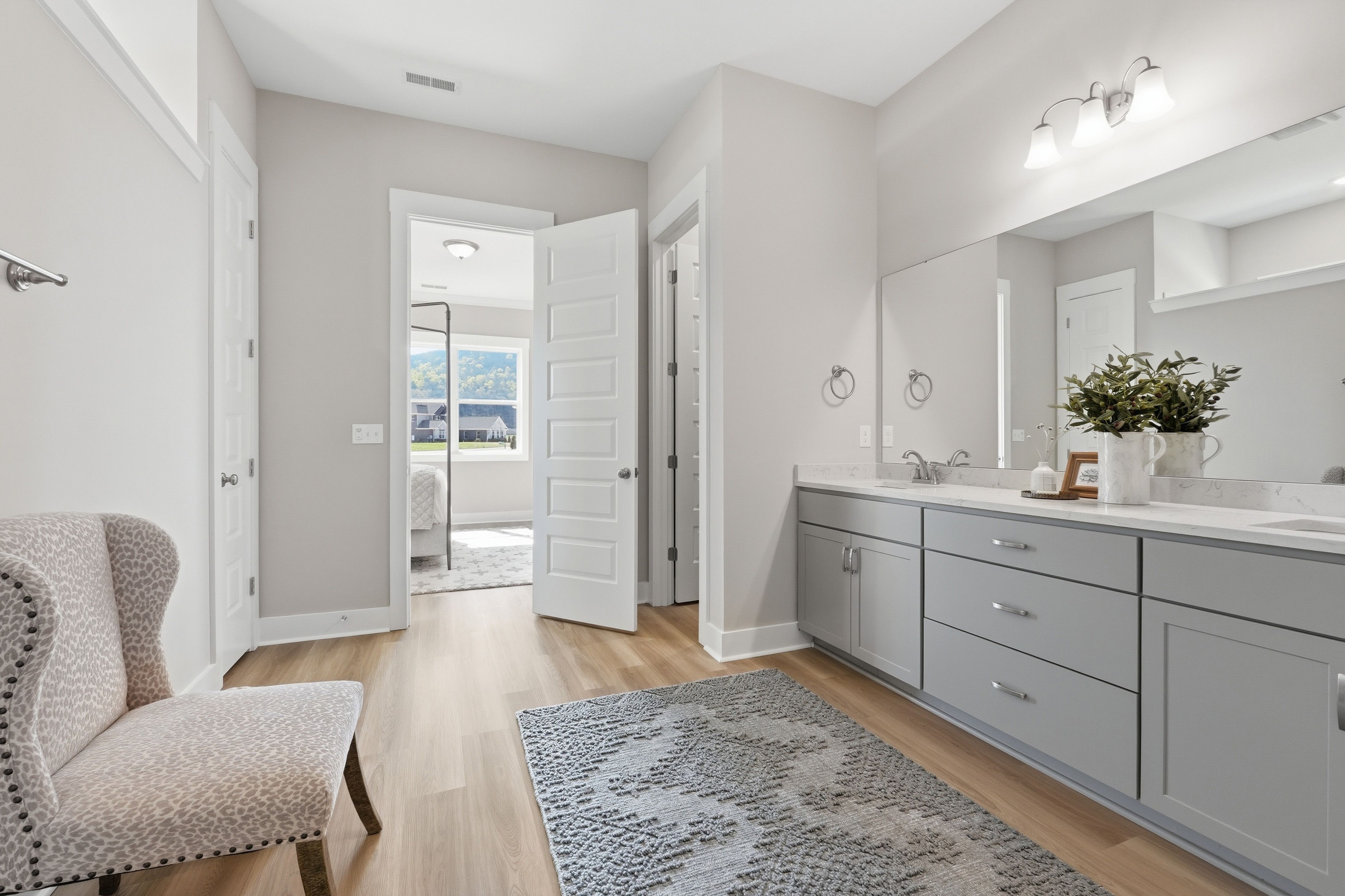 Spacious primary bathroom at The Meadows at Hampton Cove in Owens Cross Roads AL featuring gray vanity, mirror, and open bedroom door