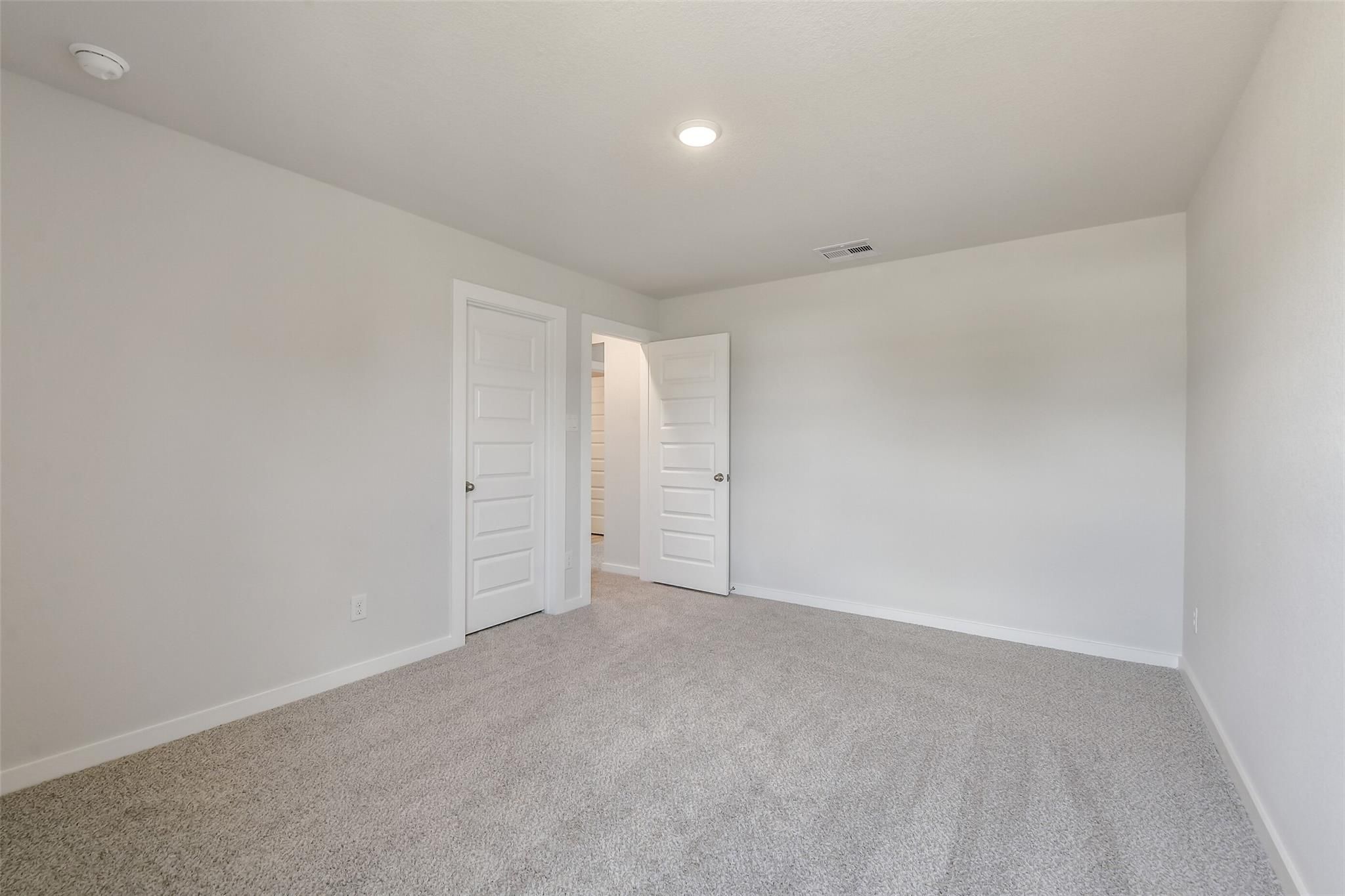 Spacious secondary bedroom with open bathroom door, gray carpet, white walls in Davidson Homes San Marcos E, Conroe Texas