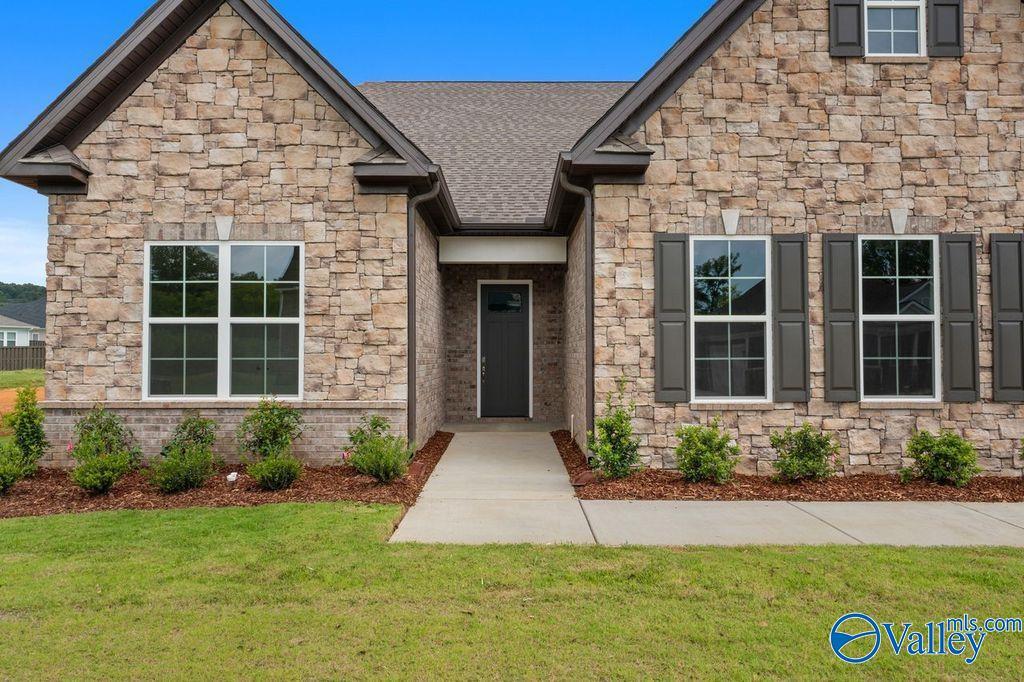 Stone-front 1.5-story home with dark shutters, front door, and landscaped walkway in The Meadows at Hampton Cove, Owens Cross Roads, Alabama - Evermore Homes The Oxford