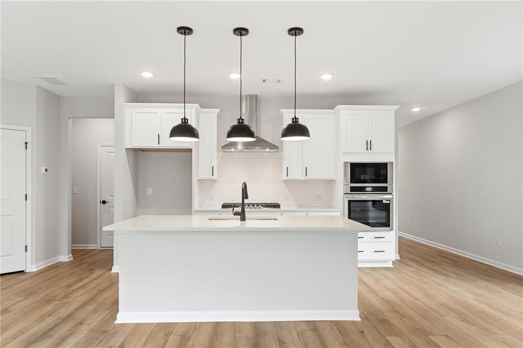 Modern white kitchen with large island, stainless steel appliances, and pendant lights in Davidson Homes The Rabun C, Winder, GA