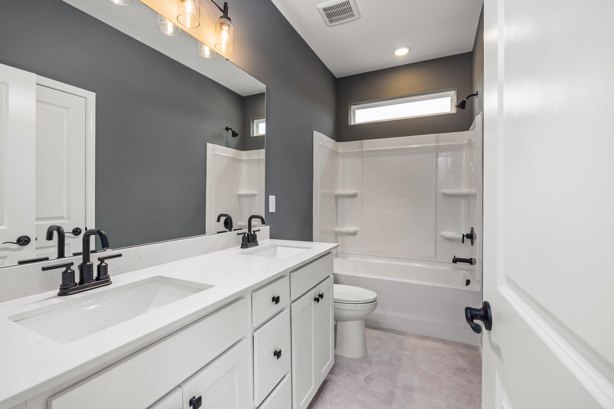 Modern bathroom in Forestville Yard, Knightdale NC with double white vanity, black faucets, bathtub, and gray walls by Davidson Homes