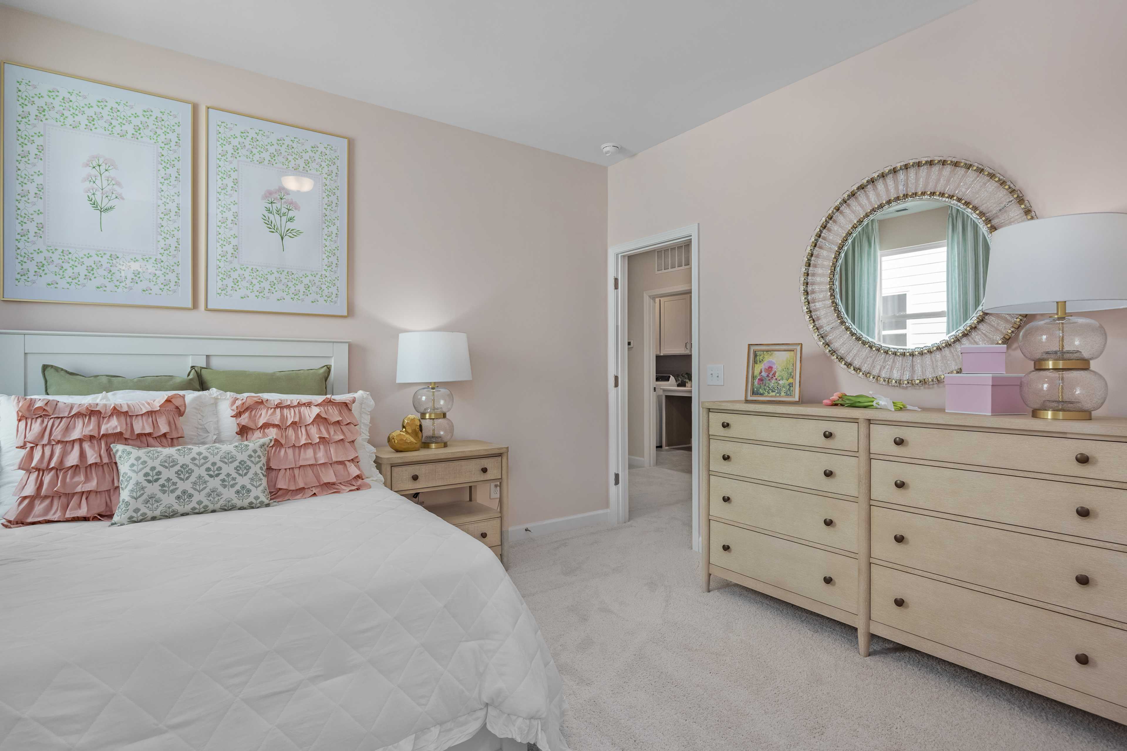 Cozy girl's bedroom at Sage on North Main in Wake Forest NC with white bed, pink walls, botanical art, gold mirror and dresser