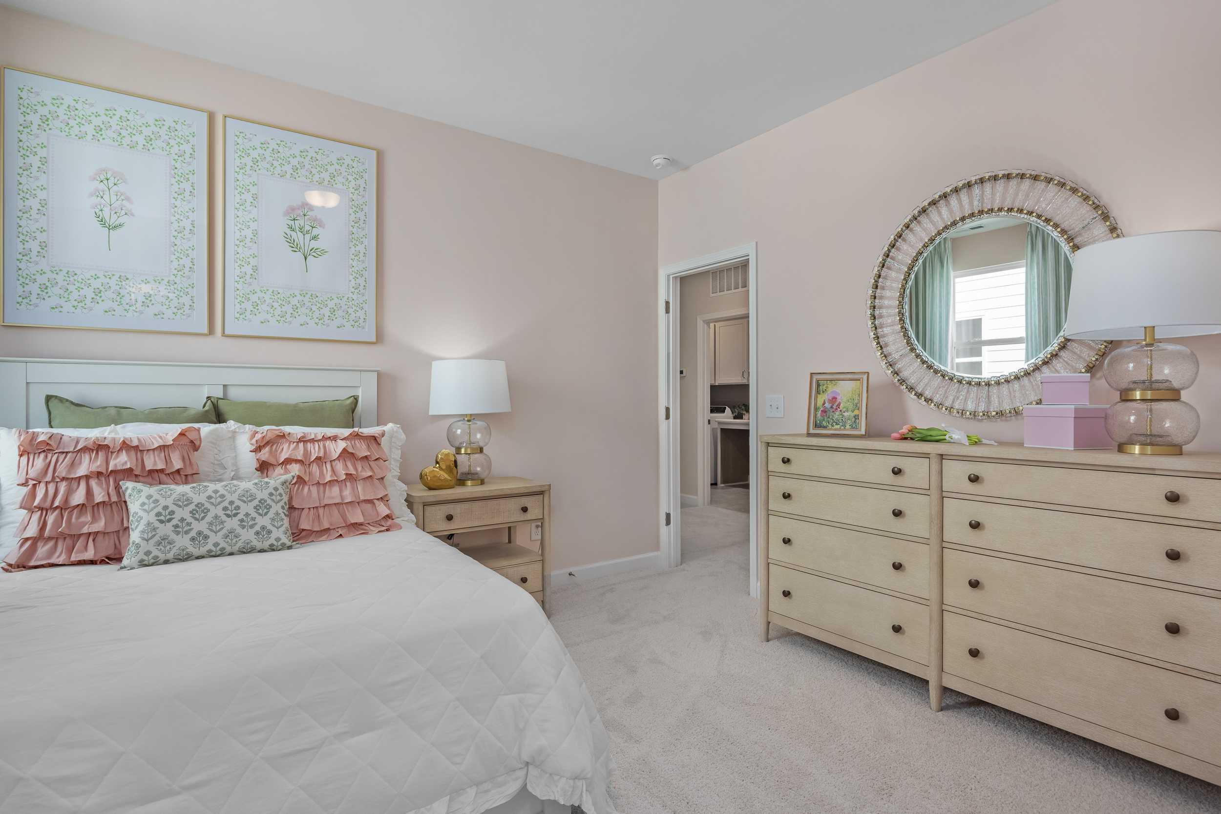 Blush pink master bedroom in The Hickory II E with king bed, botanical wall art, round mirror, and wooden dresser
