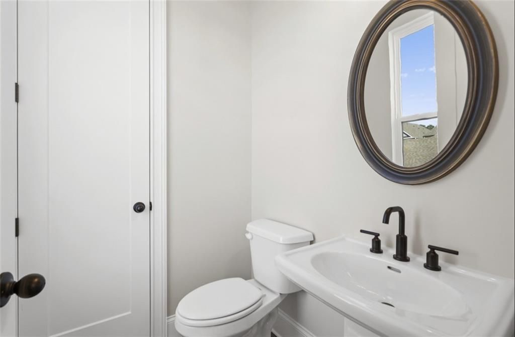 Modern powder room with white porcelain sink, toilet, black faucet, and bronze oval mirror in Davidson Homes The Seaside A, Woodstock, GA