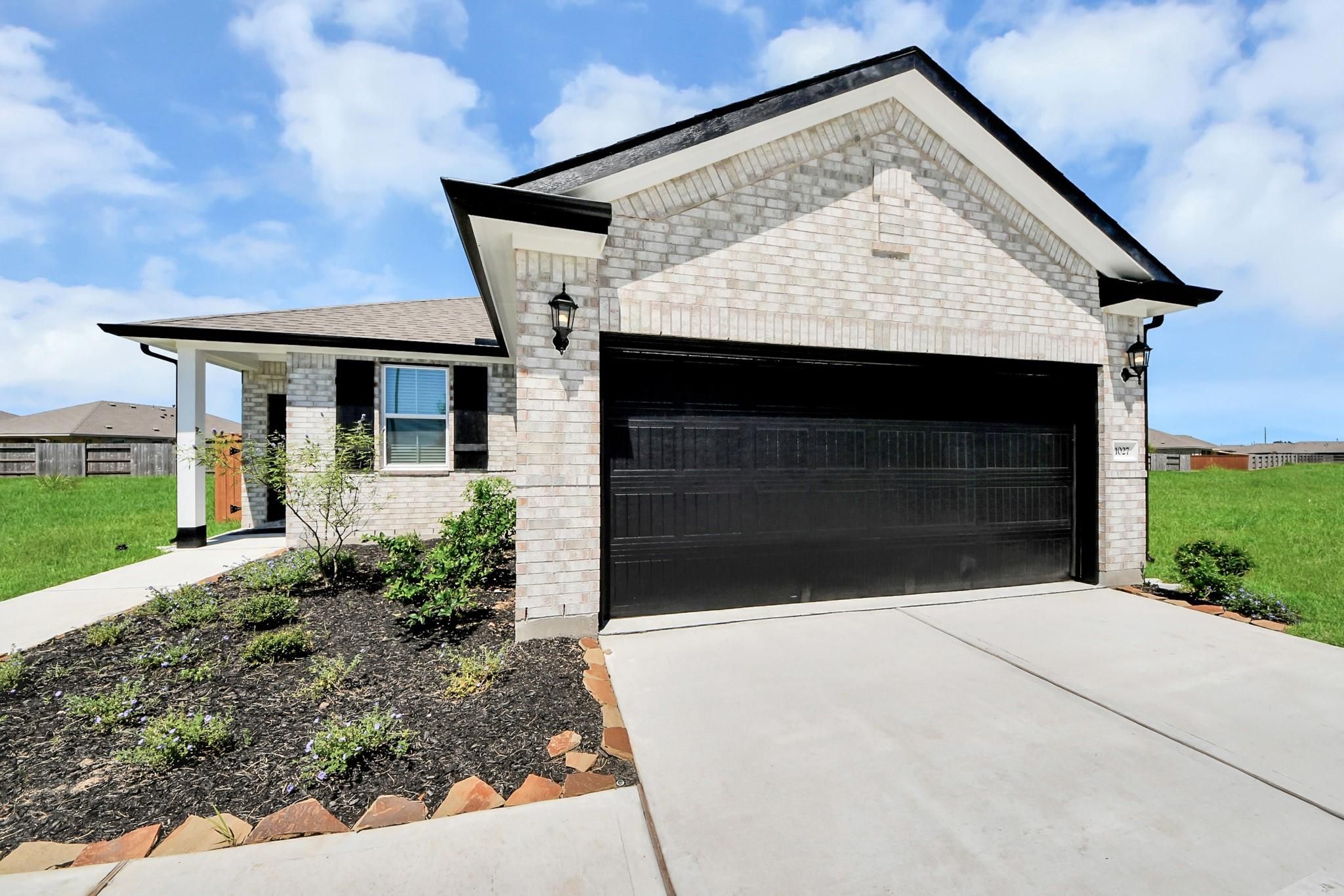 White brick exterior with black 2-car garage and landscaped beds at Davidson Homes The Costa A in Emberly, Beasley, Texas