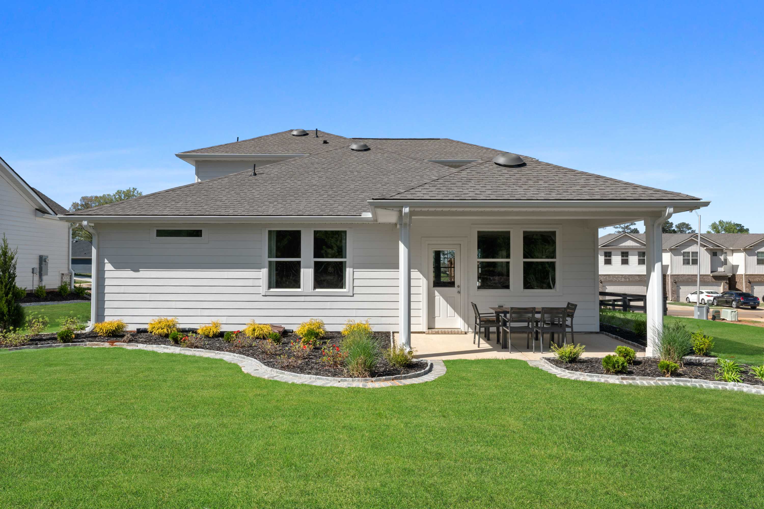 Rear view of modern home at Evergreen Mill in Madison, Alabama featuring covered patio with seating and lush landscaped yard