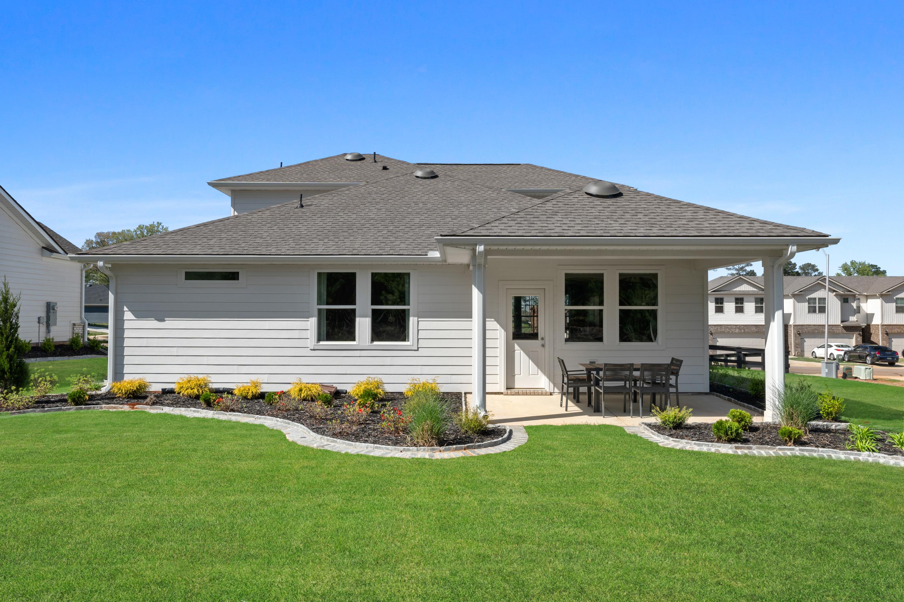 Rear view of modern home at Evergreen Mill in Madison, Alabama featuring covered patio with seating and lush landscaped yard