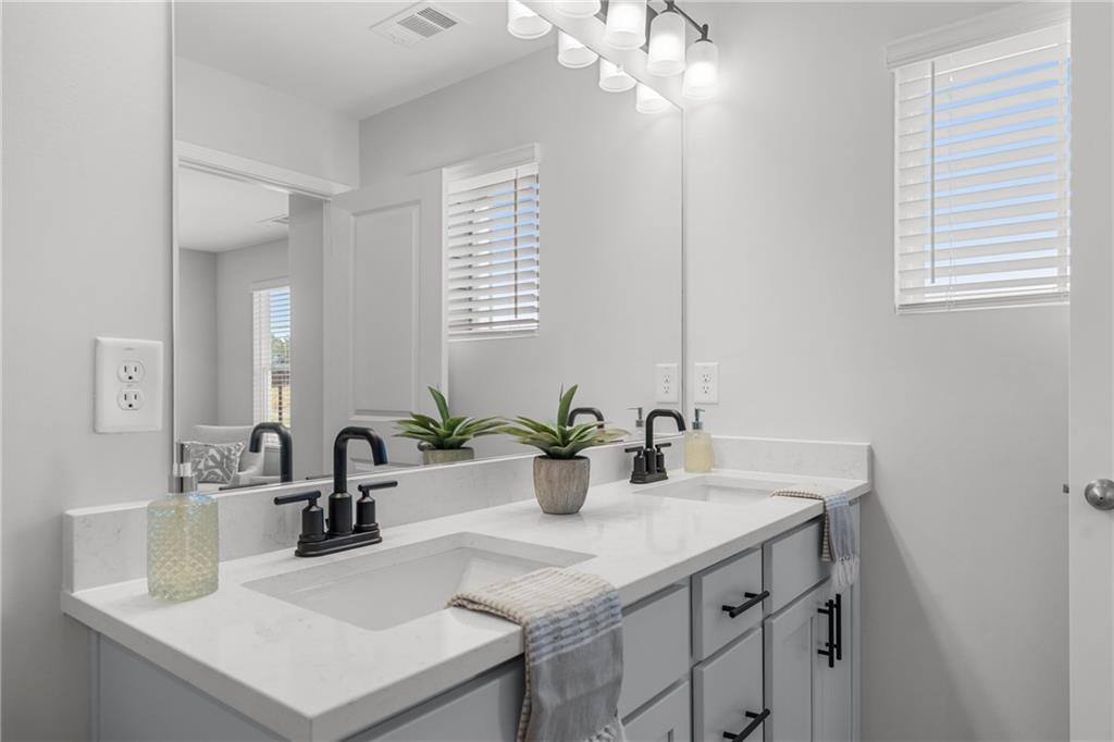 Modern double vanity bathroom with white quartz counters, black faucets, plants, and soft lighting in Davidson Homes The Durant A, Emerson, Georgia