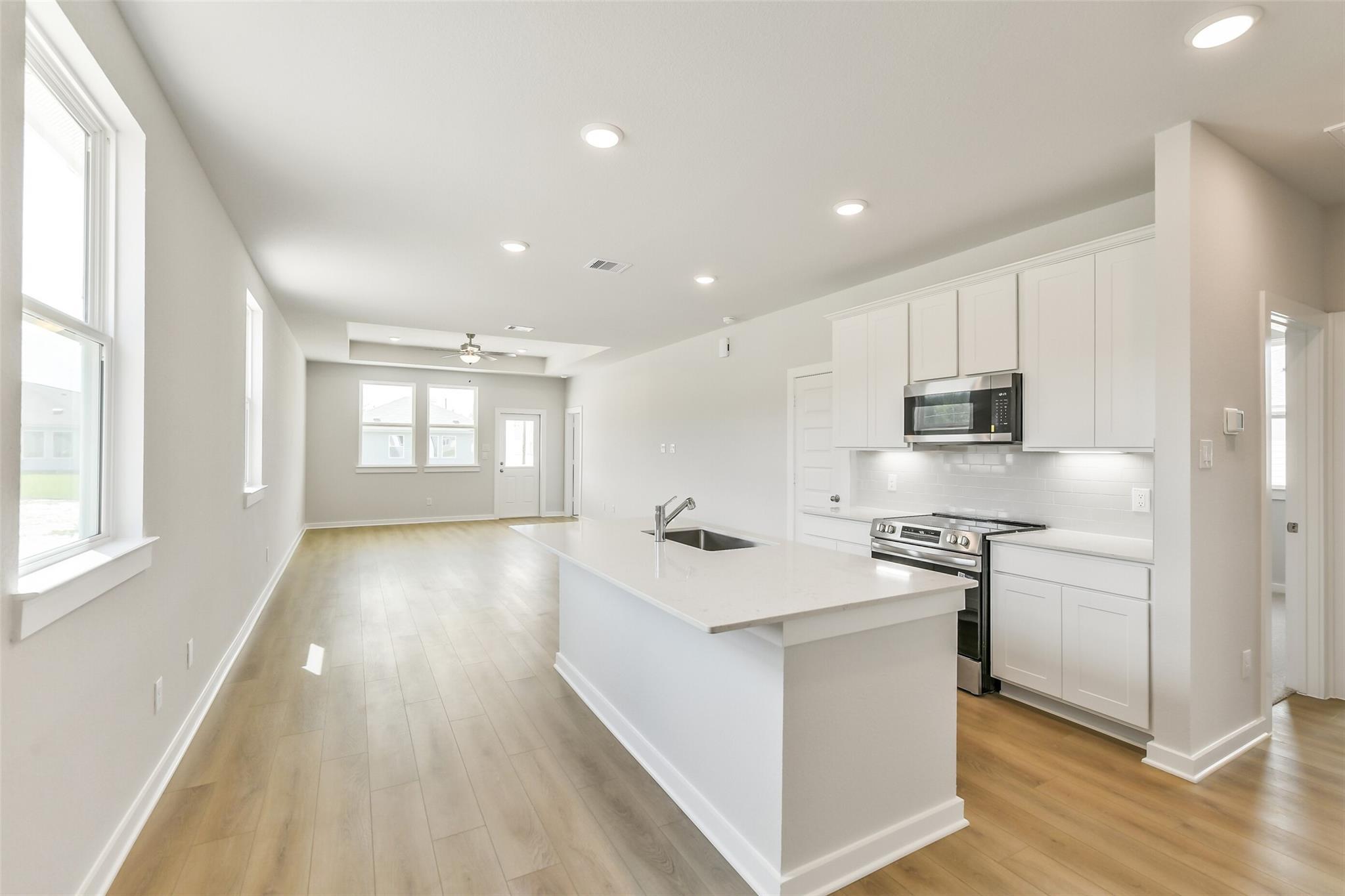 Modern open-concept kitchen with white shaker cabinets, quartz island sink, stainless appliances in Davidson Homes The Frio G, Conroe, TX