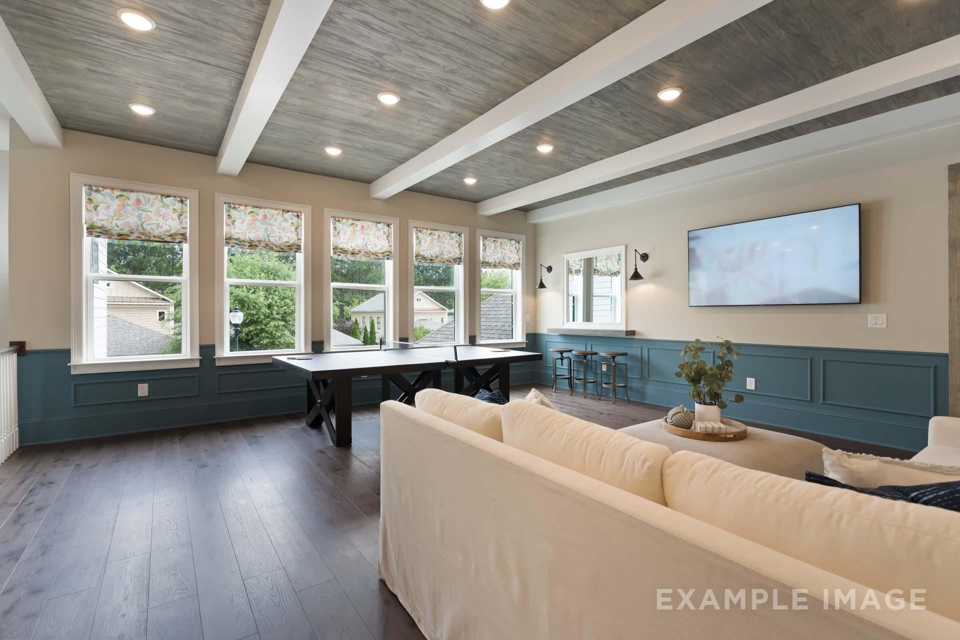 Spacious bonus room in The Seaside by Davidson Homes featuring vaulted wooden beam ceiling, ping pong table, beige sofa, and large windows