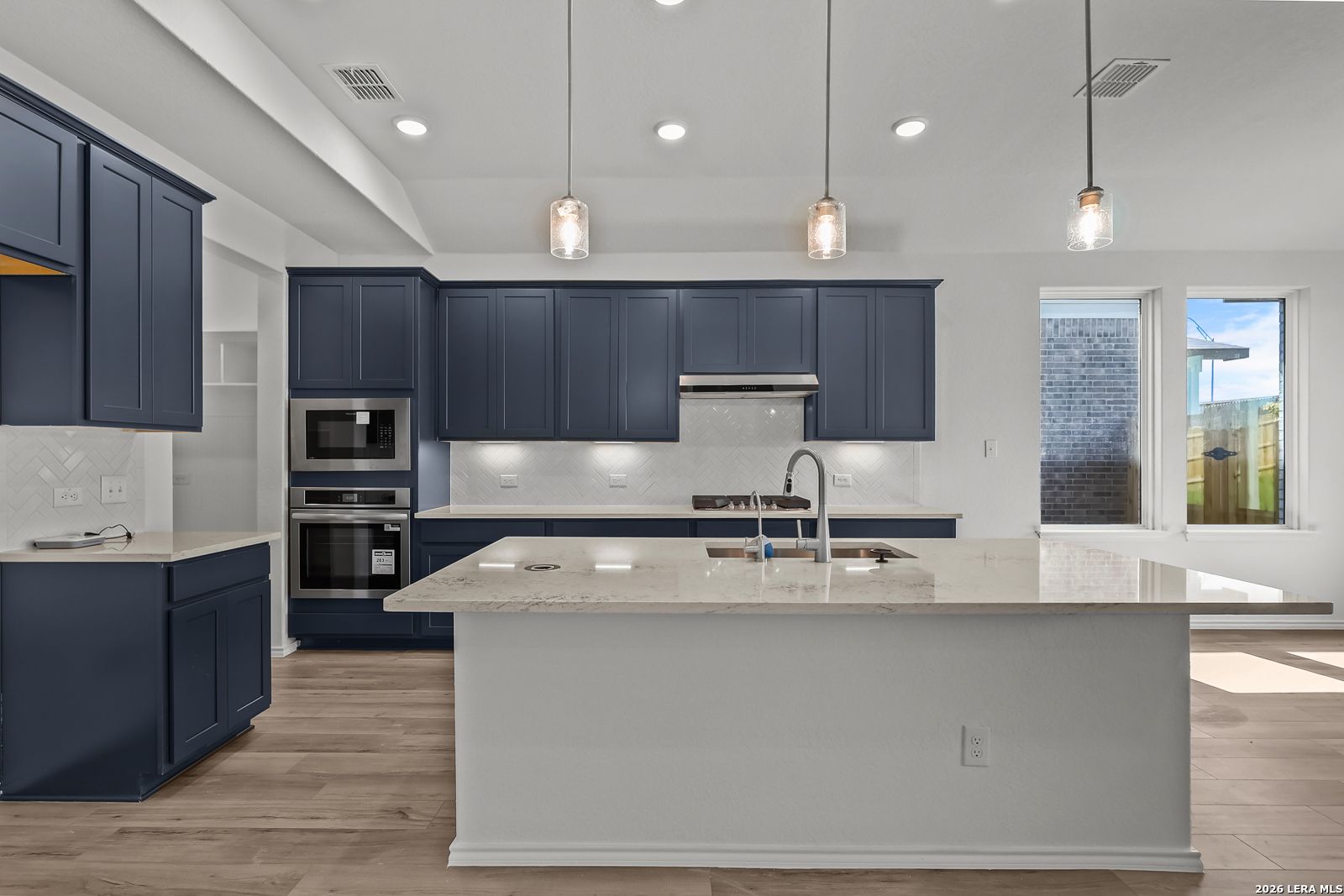 Modern navy blue kitchen cabinets, white quartz island with sink, stainless steel double oven and cooktop in Davidson Homes Sequoia B, San Antonio
