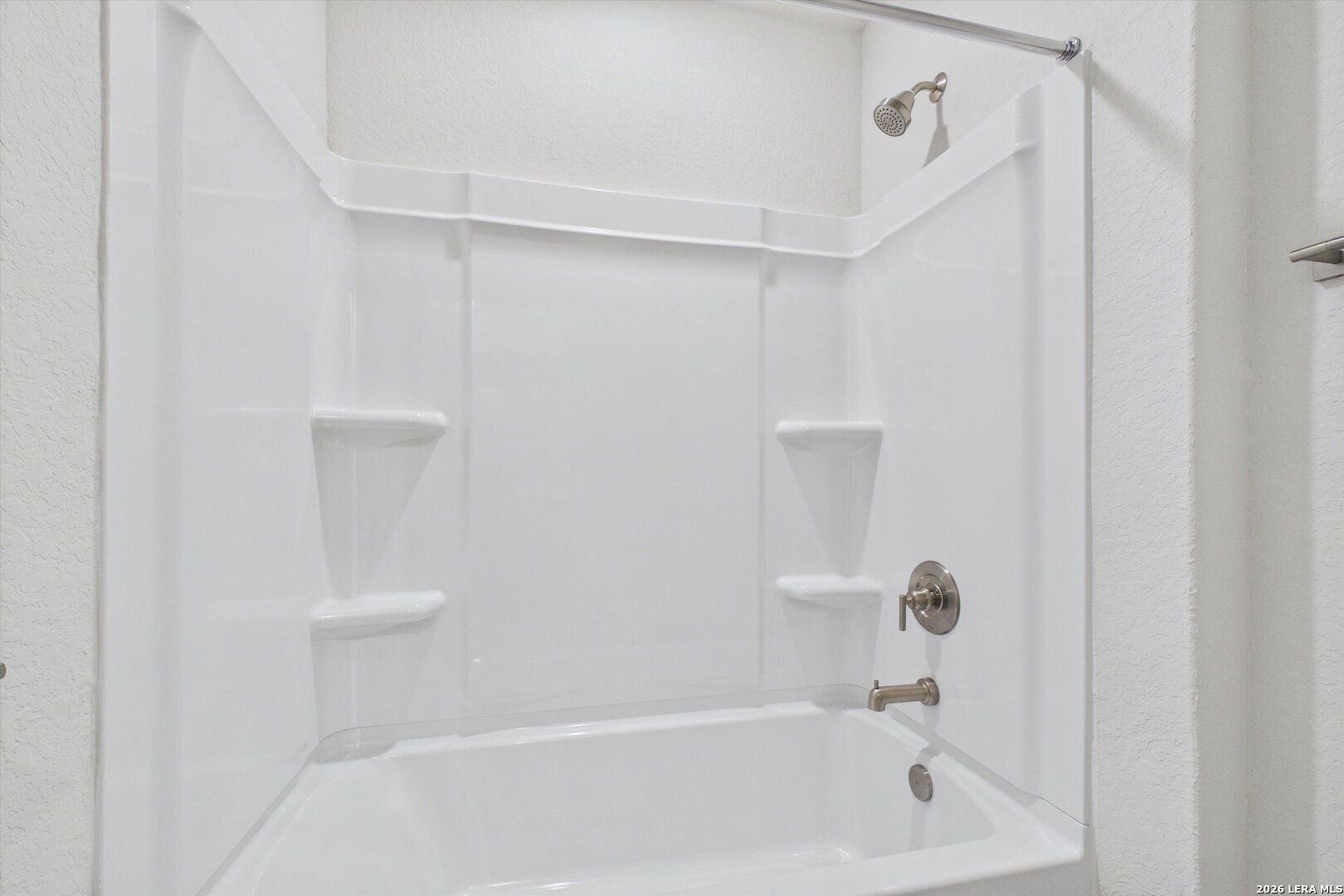 White bathtub and shower combination with built-in shelving in a Davidson Homes The Charlotte B floor plan, San Antonio.