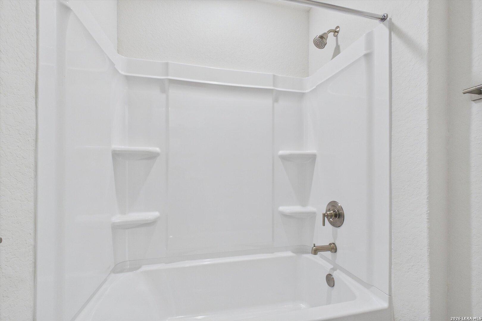 White bathtub and shower combination with built-in shelving in a Davidson Homes The Charlotte B floor plan, San Antonio.