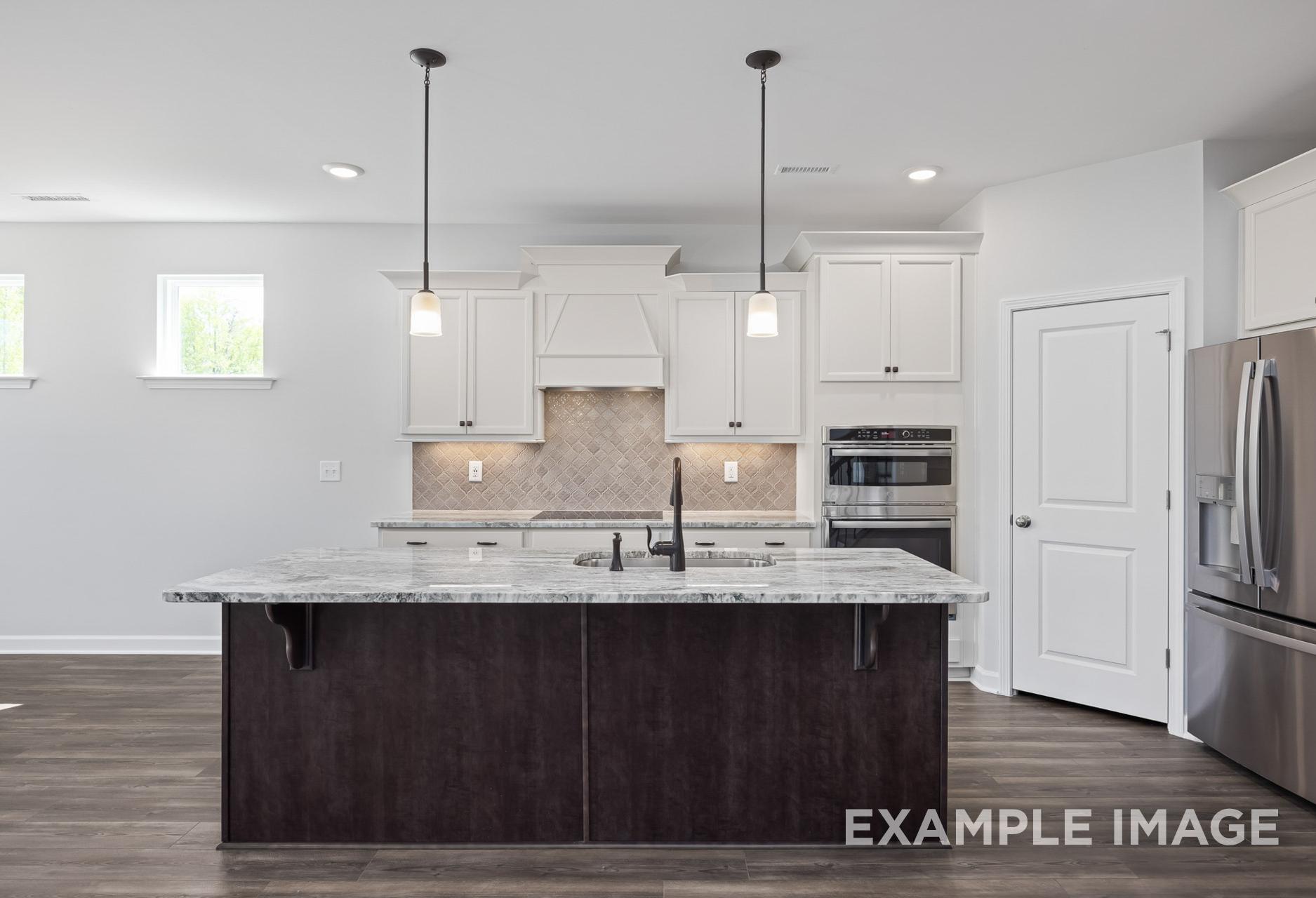Spacious kitchen in The Grace A featuring quartz island, white shaker cabinets, stainless steel appliances, pendant lights