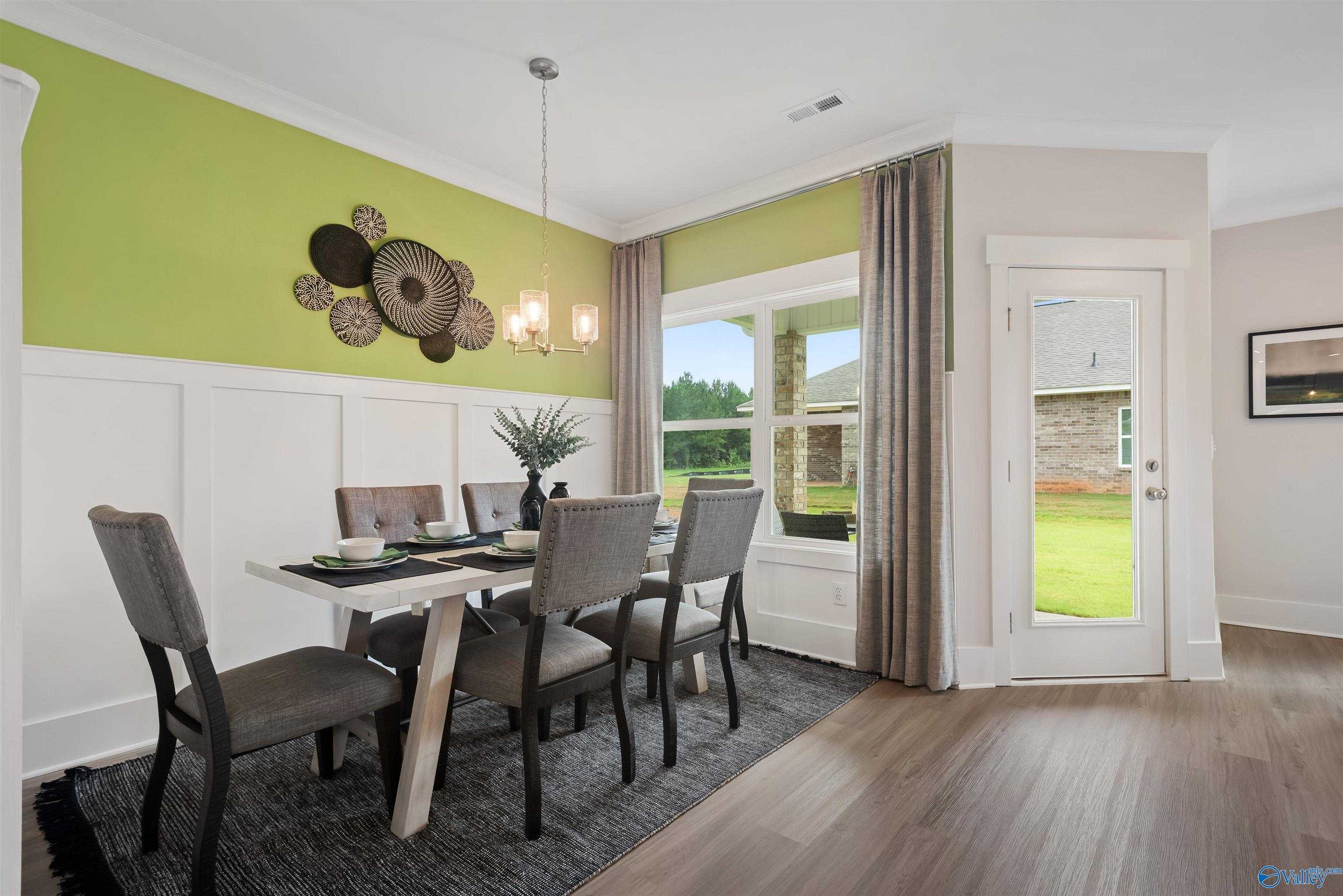 Elegant dining room with wooden table, upholstered chairs, green accent wall, and backyard view in Davidson Homes The Daphne, Harvest, Alabama
