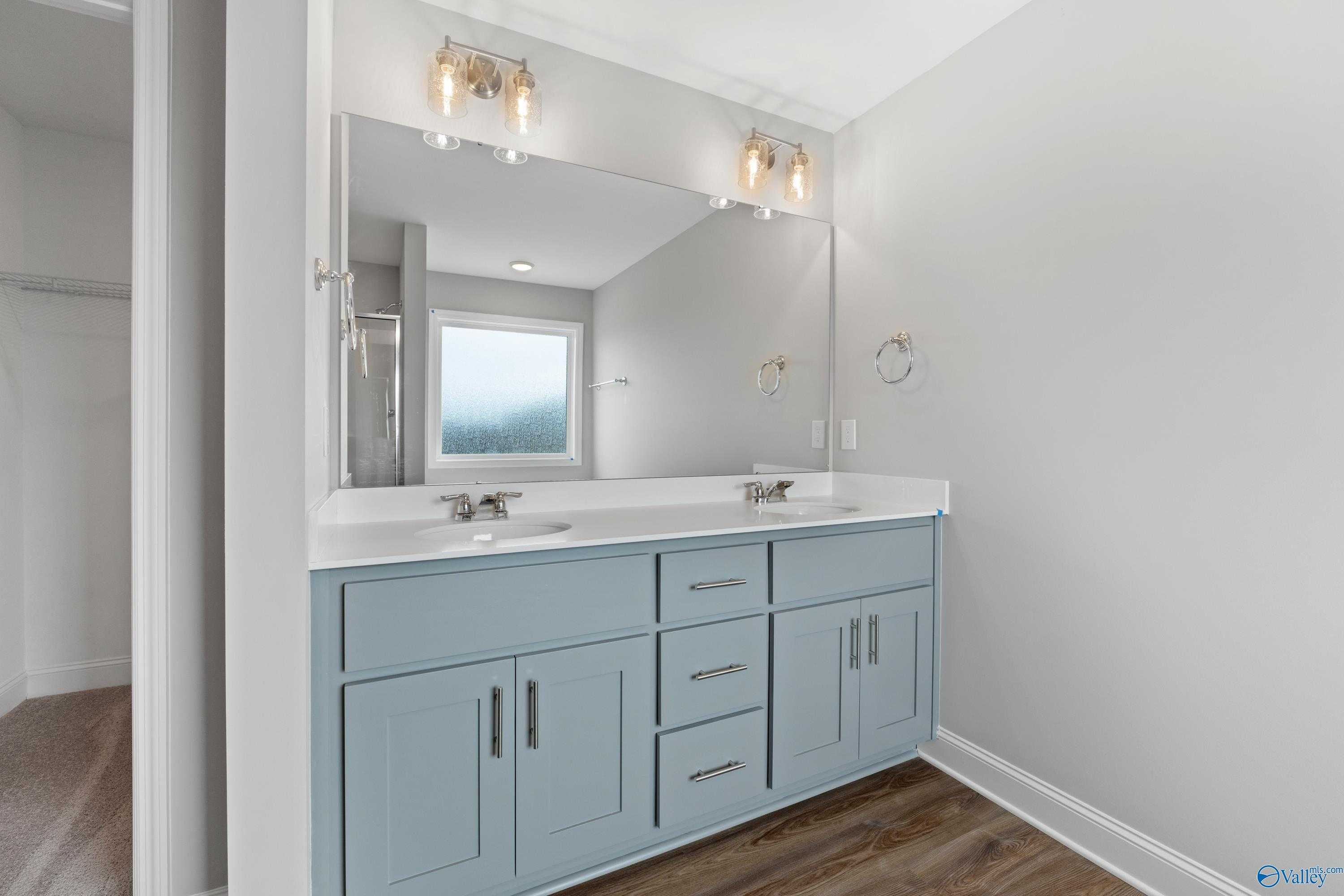 Elegant master bathroom with double vanity, light blue cabinets, mirrors, and window in Davidson Homes The Aiken, Meridianville, Alabama