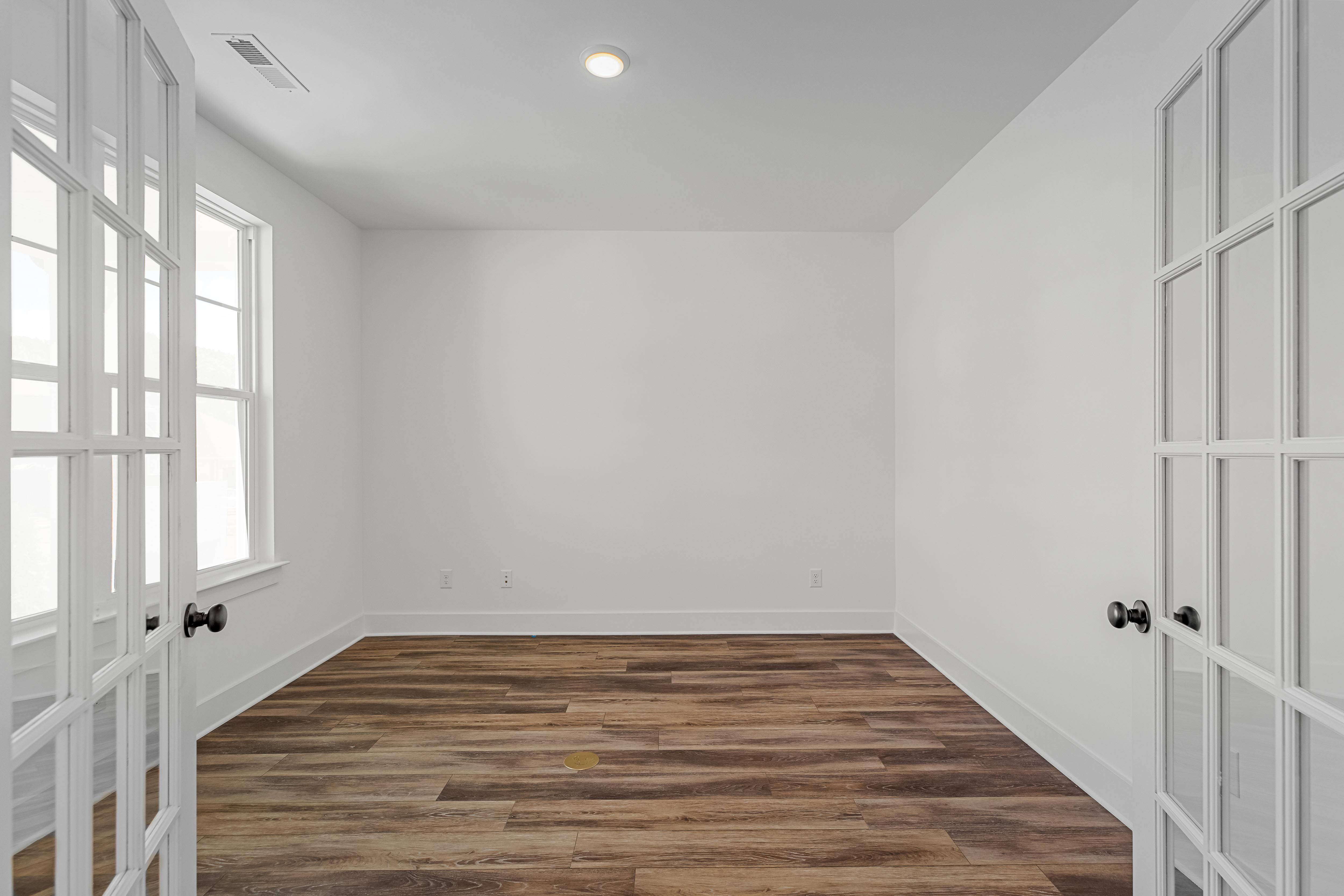 Bright home office or flex room in The Cedar by Davidson Homes featuring white walls, wood-look flooring, and French doors.