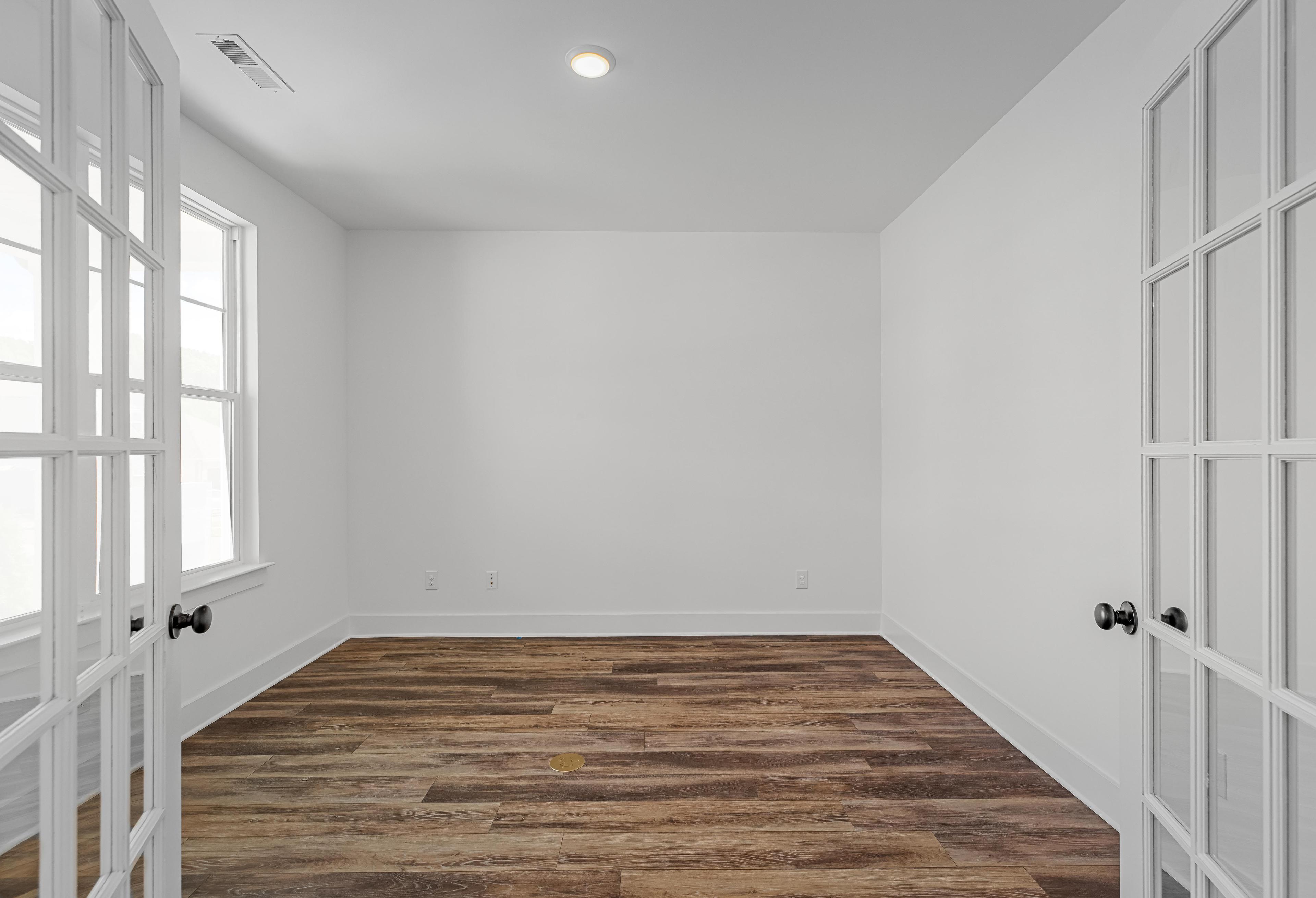 Bright home office or flex room in The Cedar by Davidson Homes featuring white walls, wood-look flooring, and French doors.