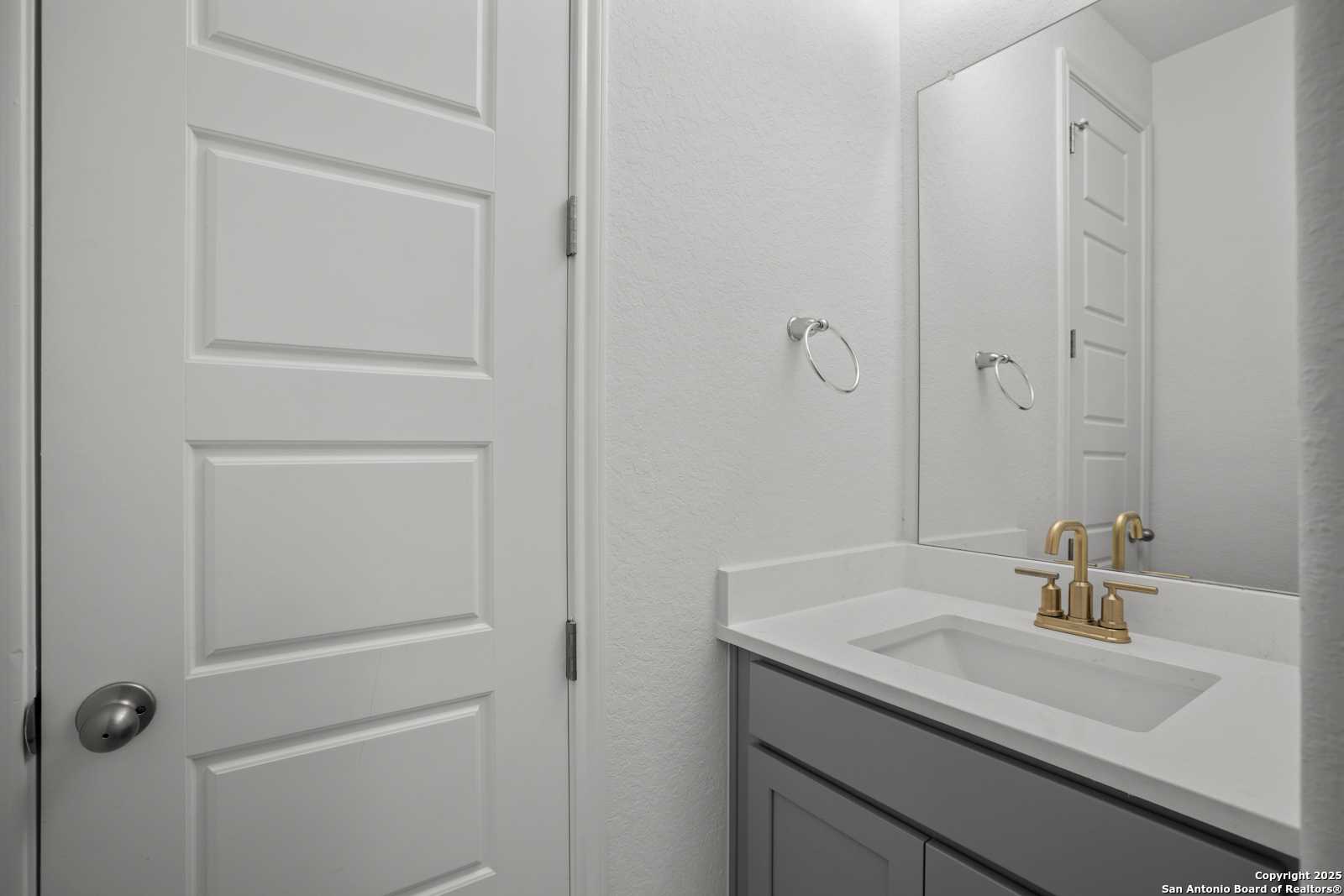 Elegant bathroom vanity with white countertop, gold faucet, large mirror, and grey cabinets in Davidson Homes The Summerlin B, Castroville, Texas