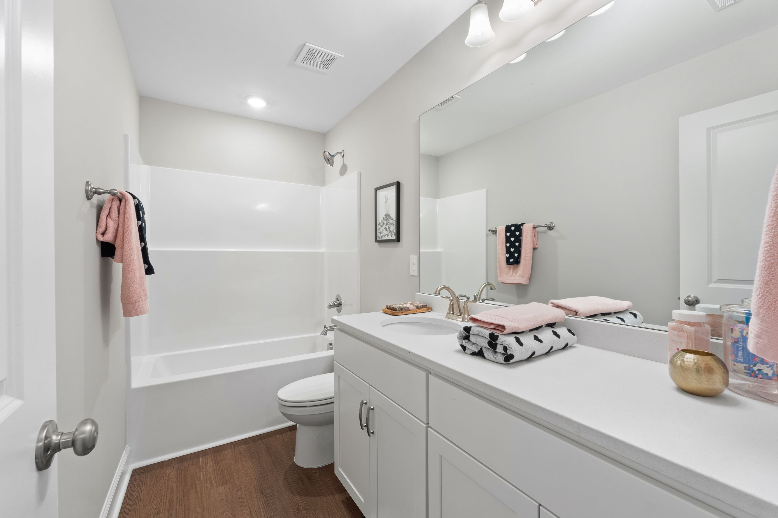 Modern secondary bathroom in The Haven D by Evermore Homes featuring white subway tile shower, soaking tub, single vanity, and pink towels