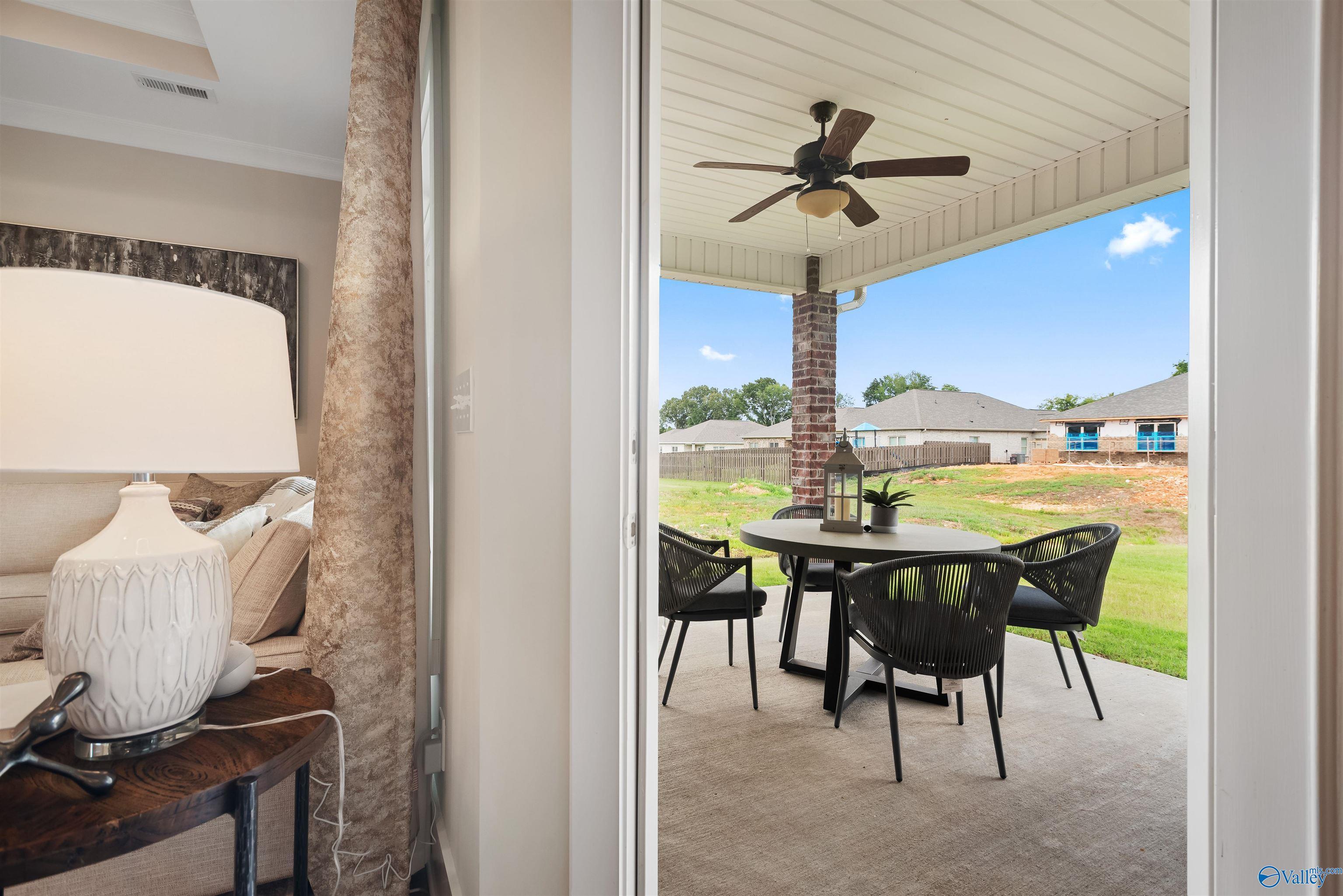 Covered back patio with ceiling fan, wicker dining set, and lush green yard view in Davidson Homes The Everett, New Market, Alabama