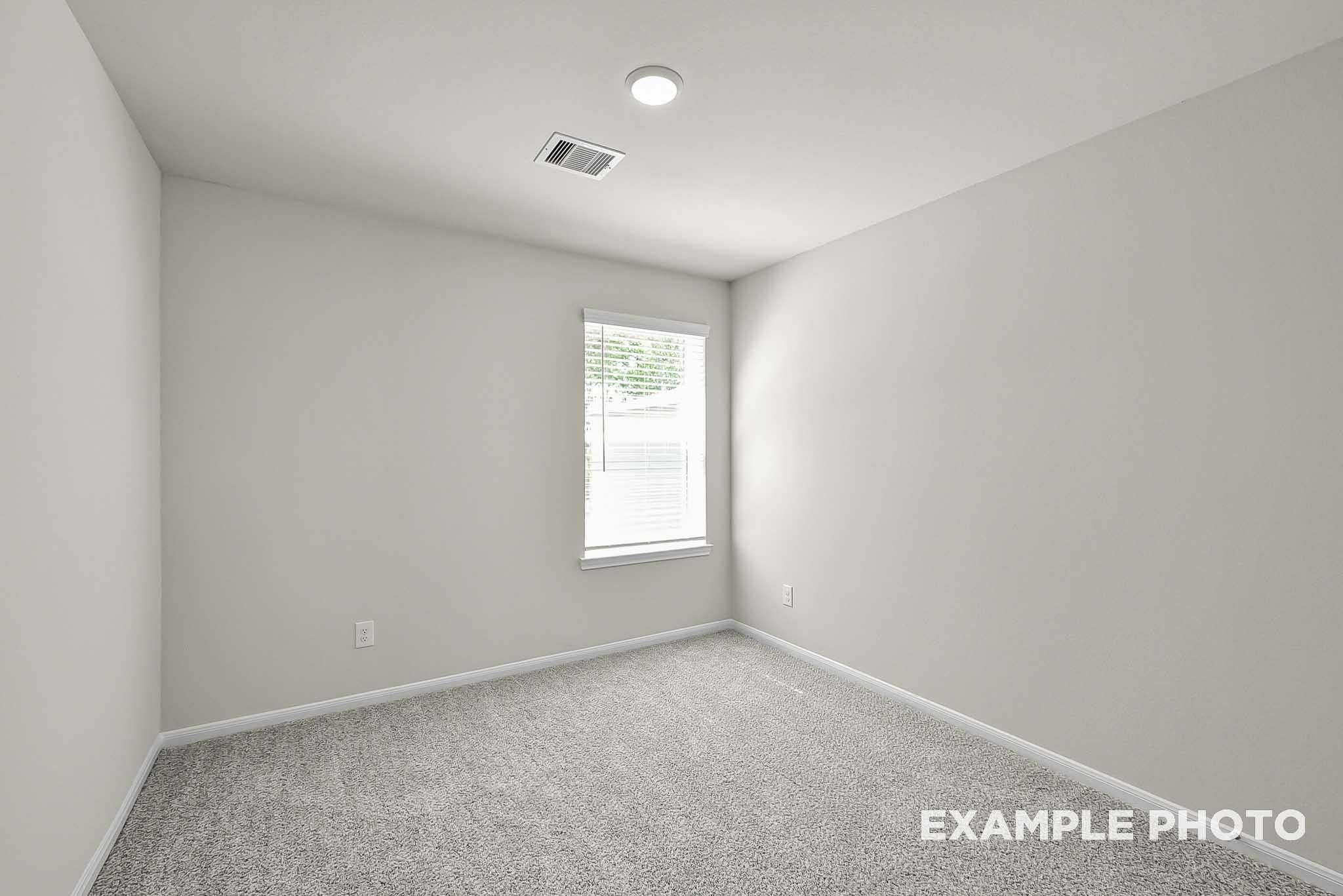 Bright, carpeted bedroom with neutral walls in The Blanco F floor plan at Spring Branch Crossing in Conroe, Texas.