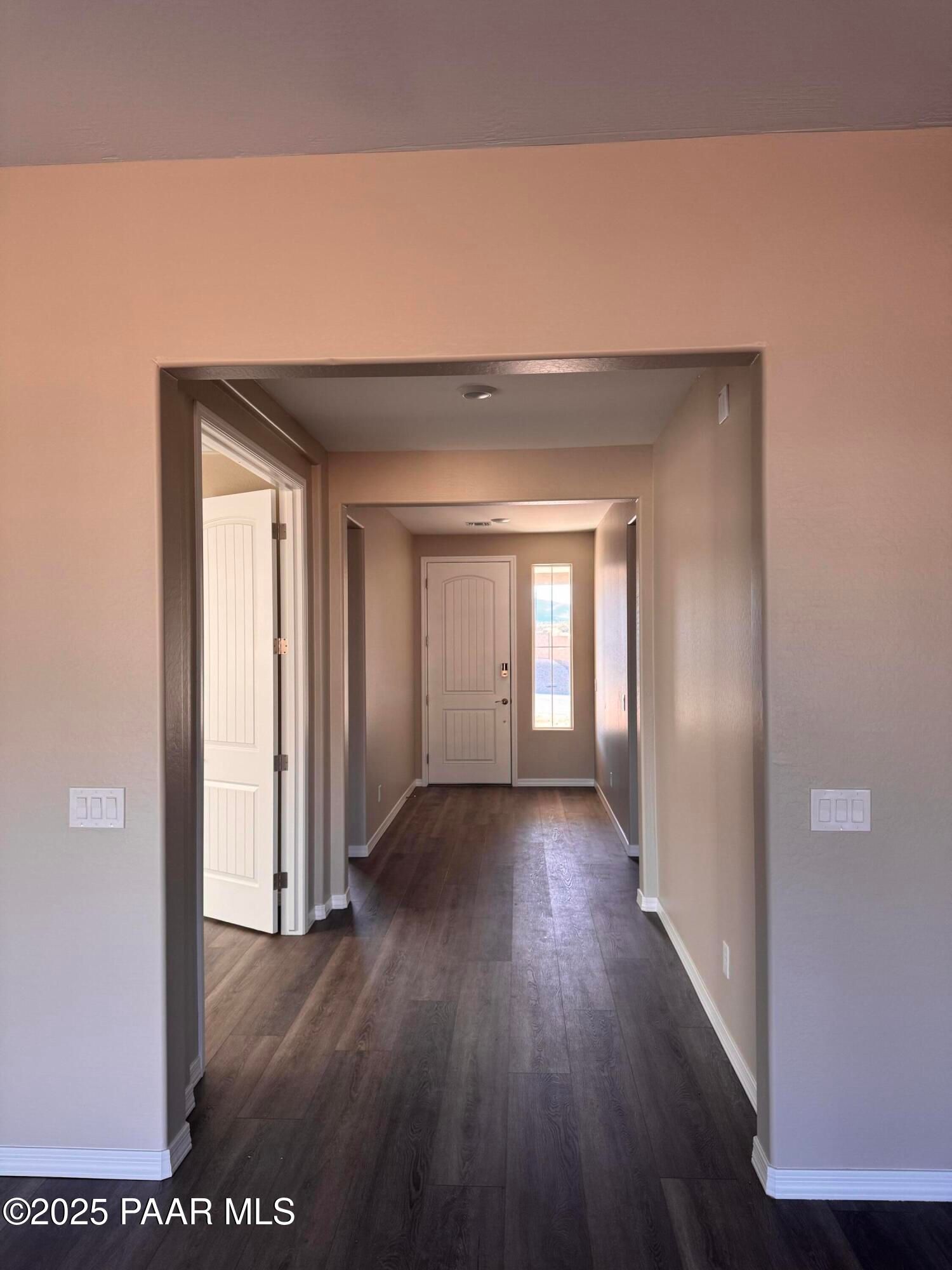 Spacious hallway with tan walls, dark laminate flooring, open side door, and white front entry with sidelight in Davidson Homes Sunrise II A, Prescott AZ