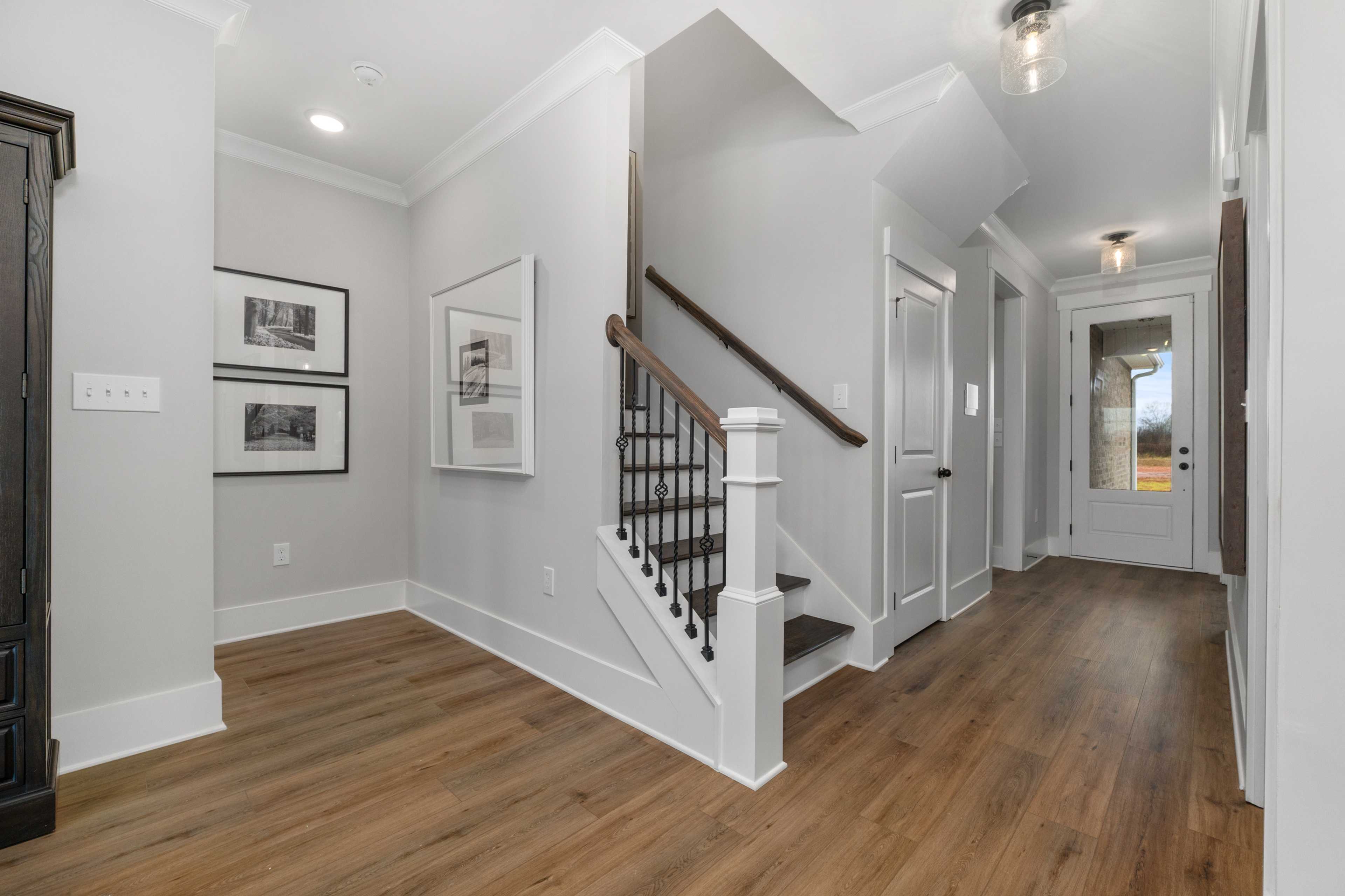 Spacious foyer with light gray walls, hardwood floors, and wrought-iron staircase at Kendall Farms in Toney, Alabama