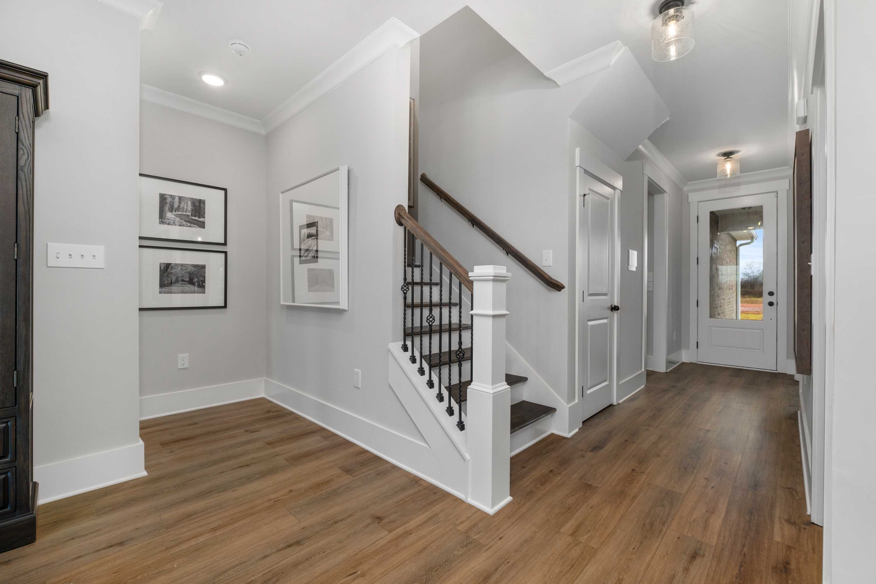 Spacious foyer with light gray walls, hardwood floors, and wrought-iron staircase at Kendall Farms in Toney, Alabama