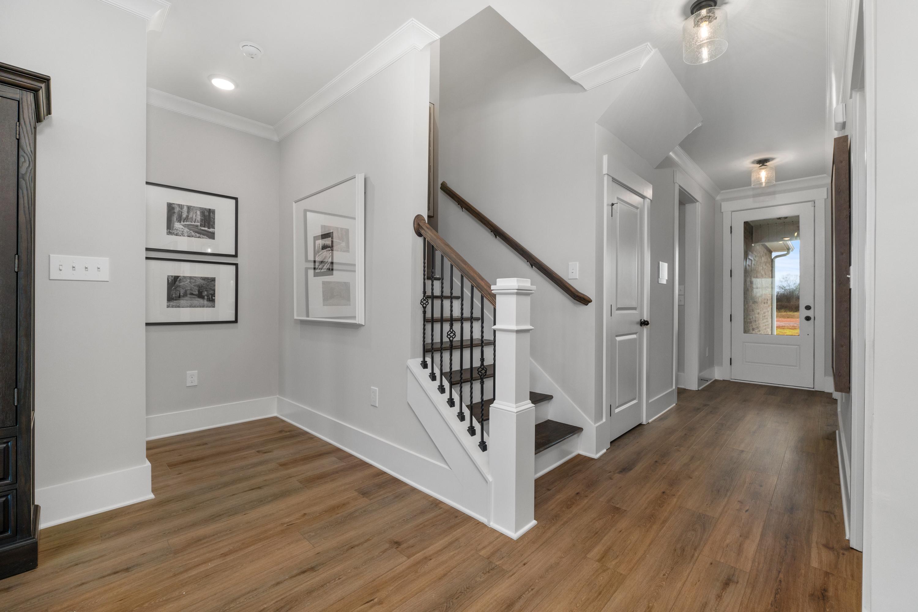 Spacious foyer with light gray walls, hardwood floors, and wrought-iron staircase at Kendall Farms in Toney, Alabama