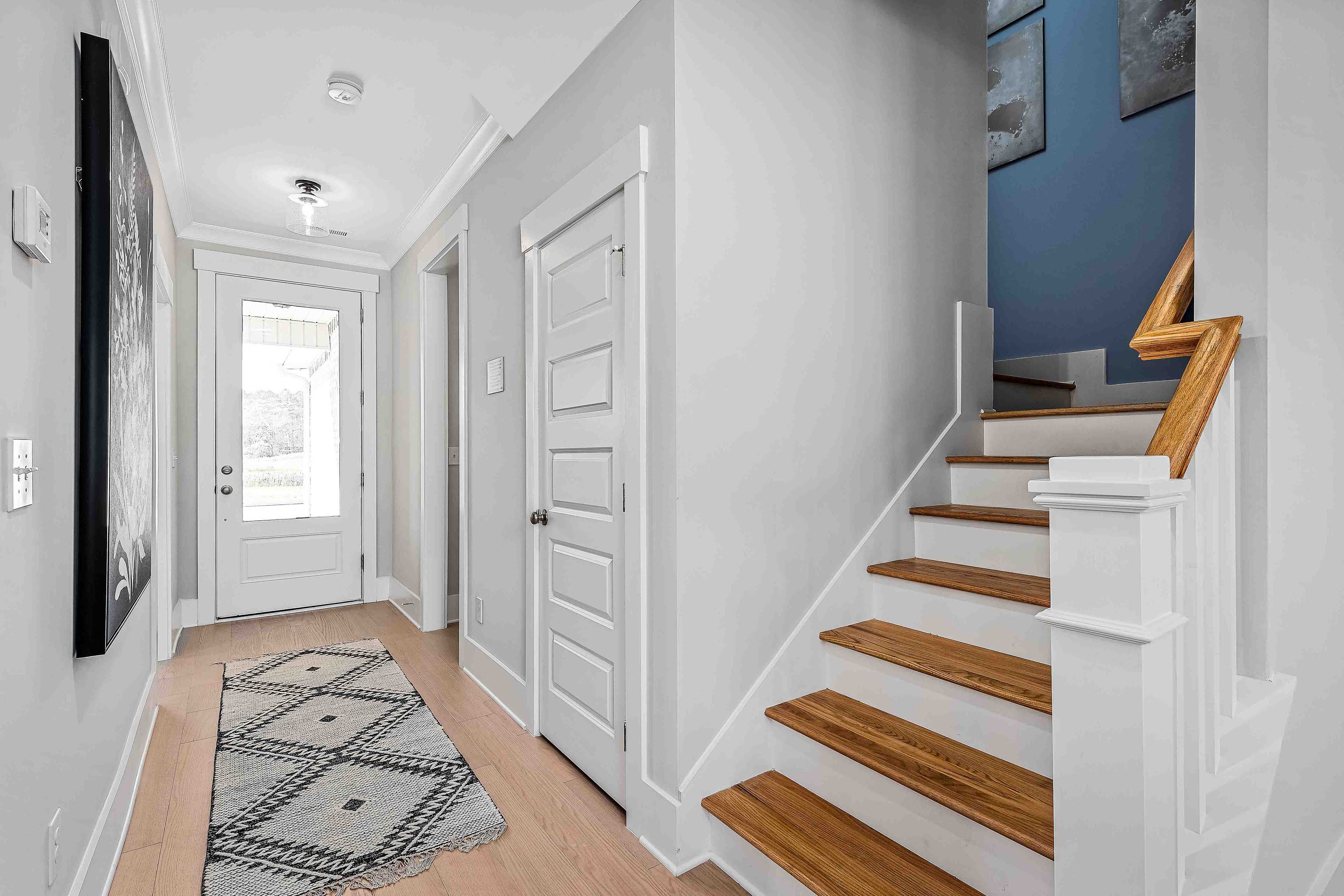 Bright entryway in Cain Park Hartselle AL home with oak staircase, gray walls, blue accent, and abstract art