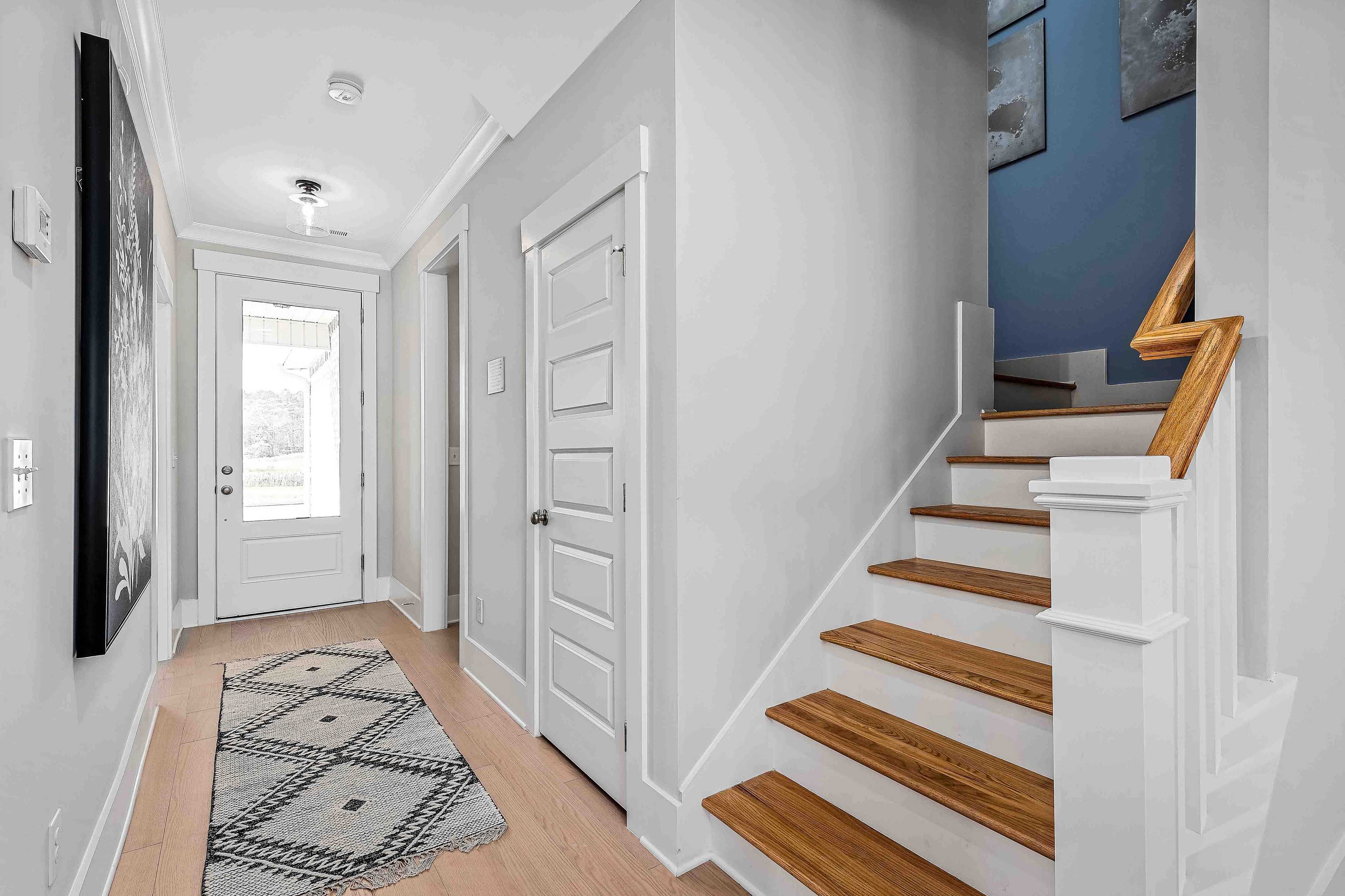 Bright entryway in Cain Park Hartselle AL home with oak staircase, gray walls, blue accent, and abstract art