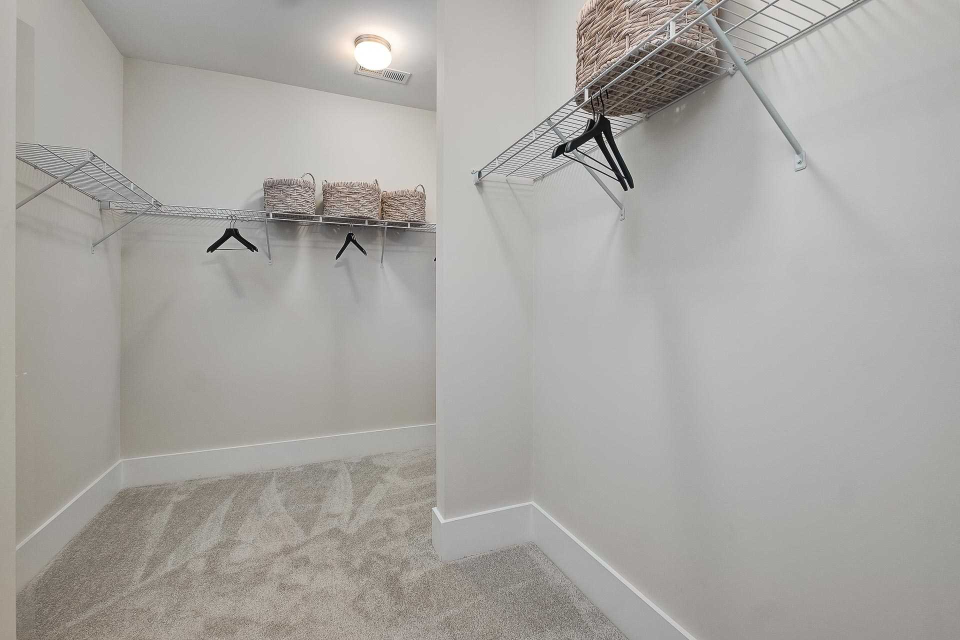 Spacious master walk-in closet in The Everett C with wire shelving, hanging rods, wicker baskets, beige walls, carpet floor