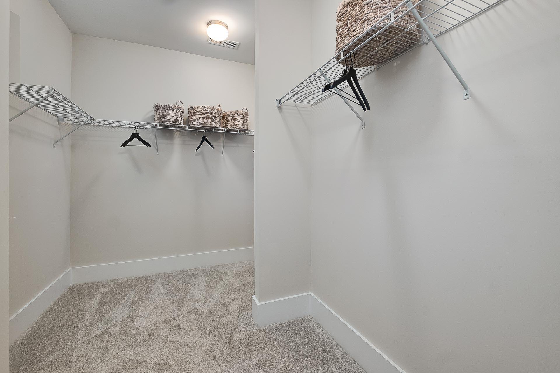 Spacious walk-in closet in The Everett master suite with wire shelving, hanging rods, woven baskets, and neutral beige tones
