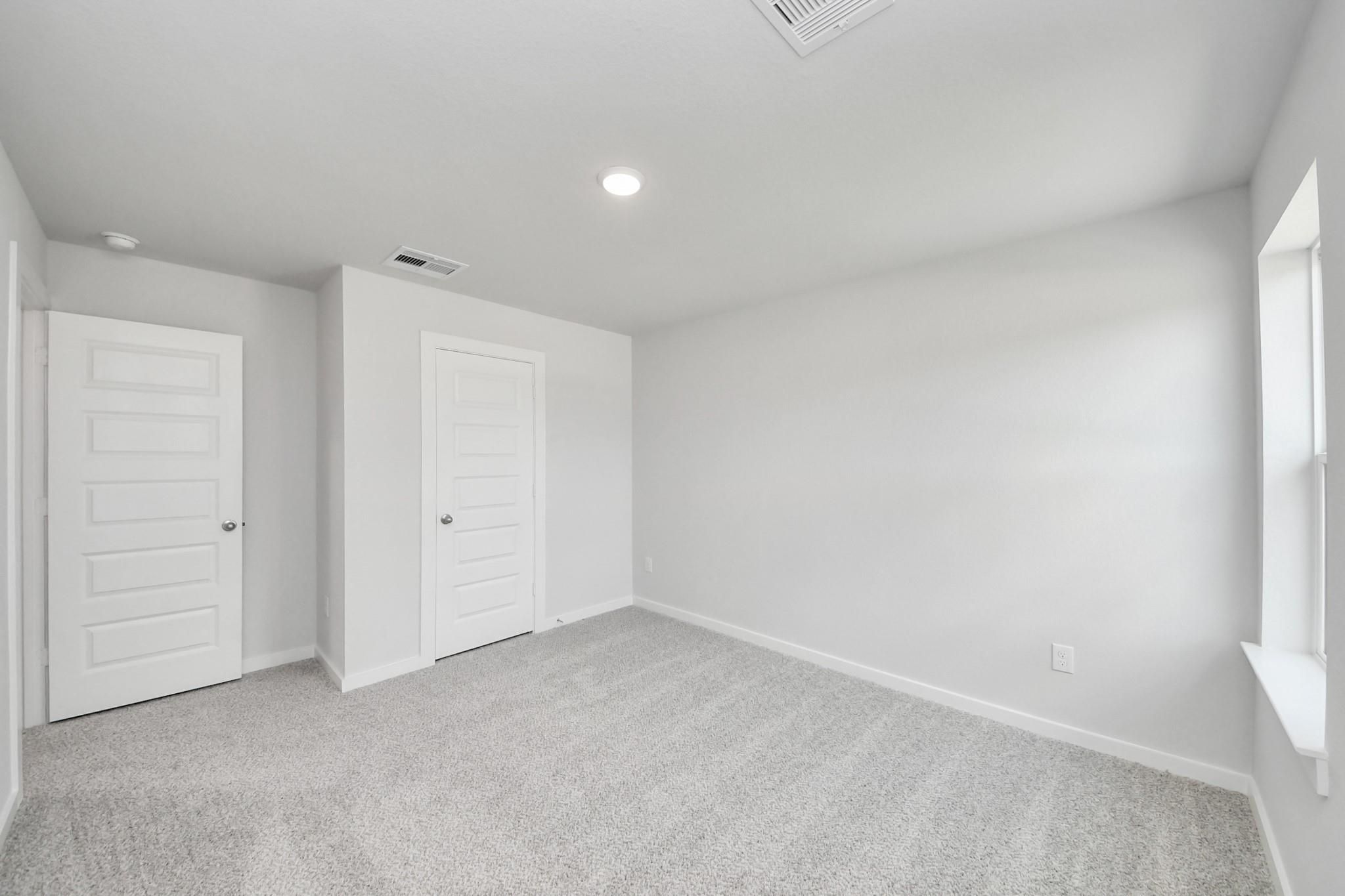 Bright, carpeted bedroom with white walls in The Sabine F floor plan at Liberty Estates, Cleveland, Texas.