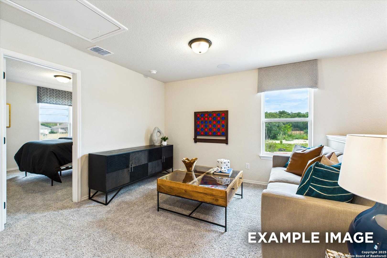 Cozy secondary bedroom with queen bed, beige sofa, dresser, and scenic backyard view in Davidson Homes The Florence C, San Antonio