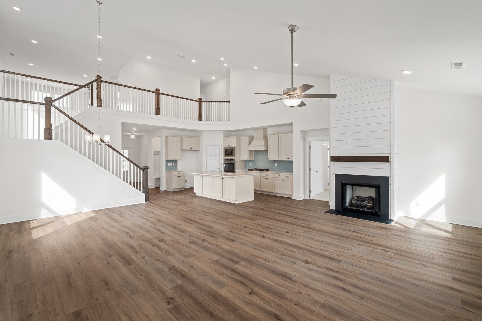 Spacious open-concept kitchen and living area with hardwood floors, white cabinets, fireplace, and staircase in Davidson Homes The Ridgeport, Gallatin, Tennessee