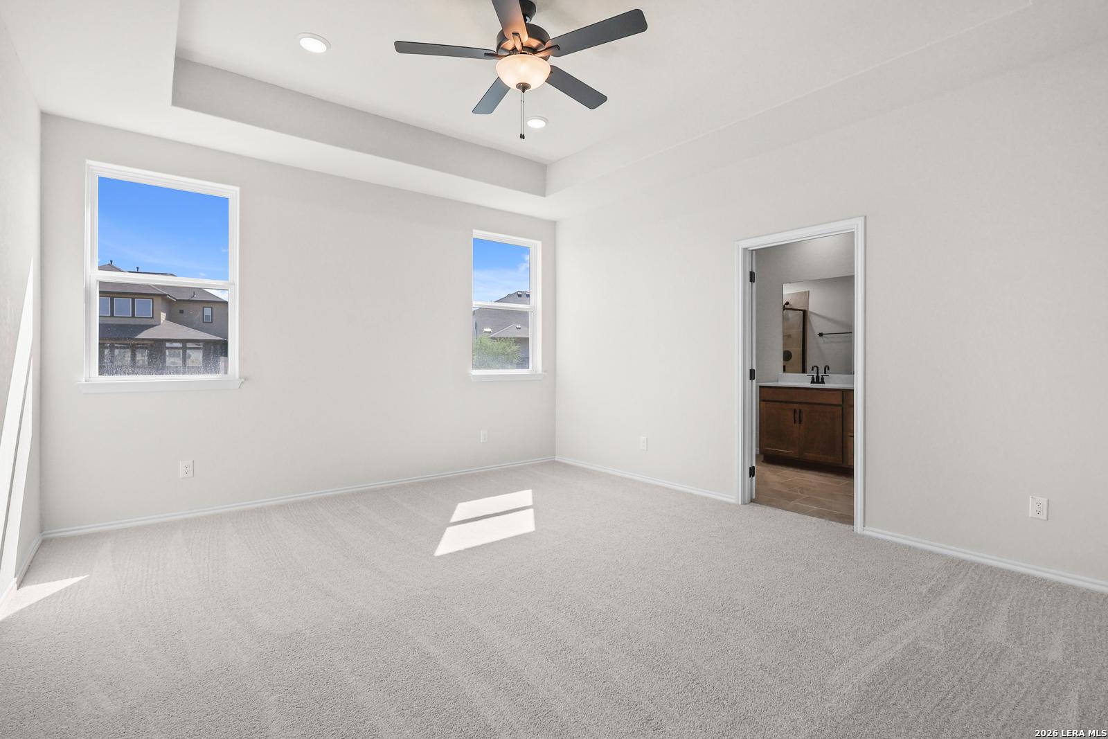 Bright primary bedroom with tray ceiling, ceiling fan, and carpet in Davidson Homes The Glenwood E, Comanche Ridge, San Antonio
