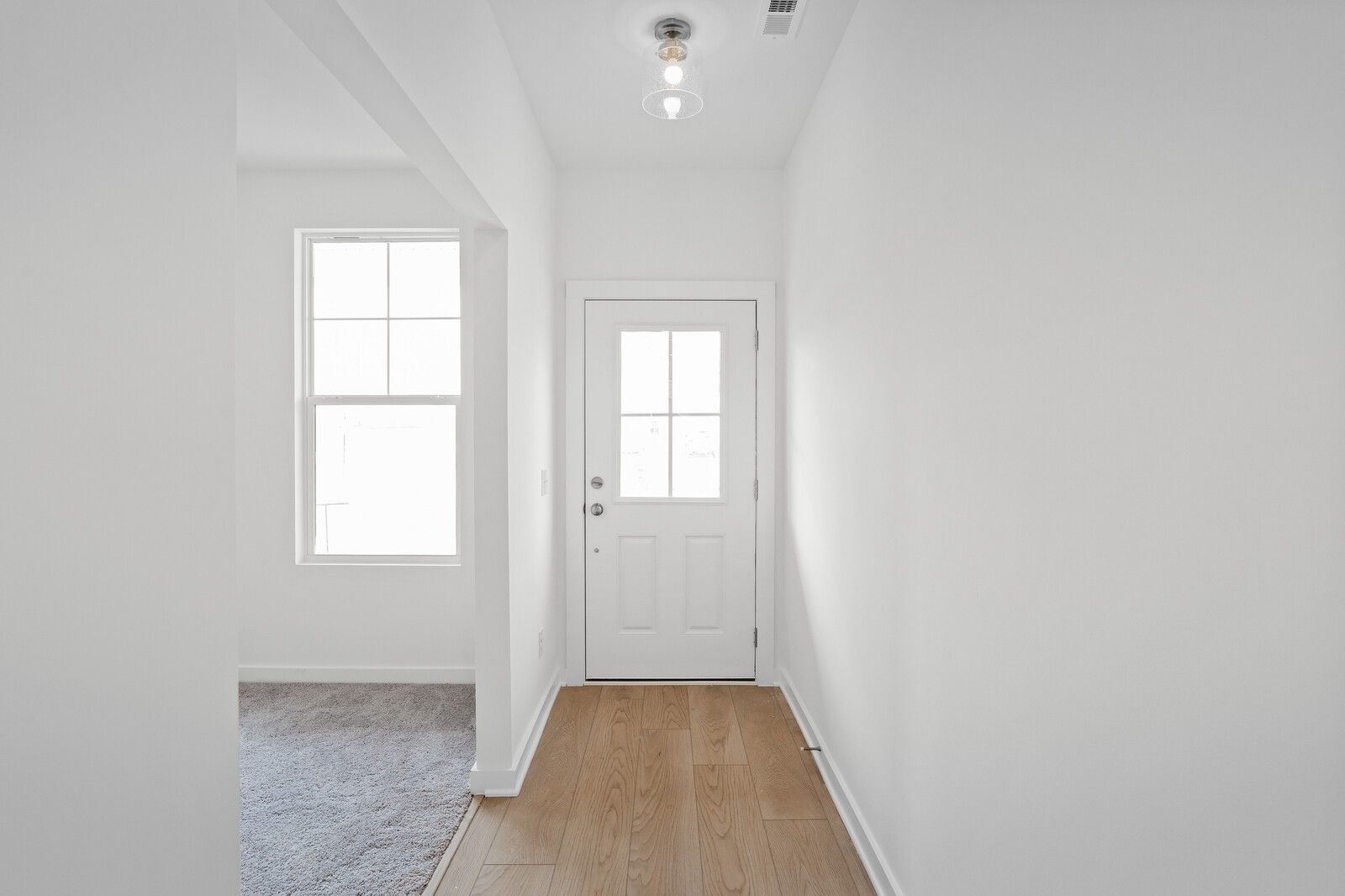 Bright hallway with oak hardwood floors, white glass-paneled door, and open archway in Davidson Homes The Logan B, Calista Farms, White House, TN