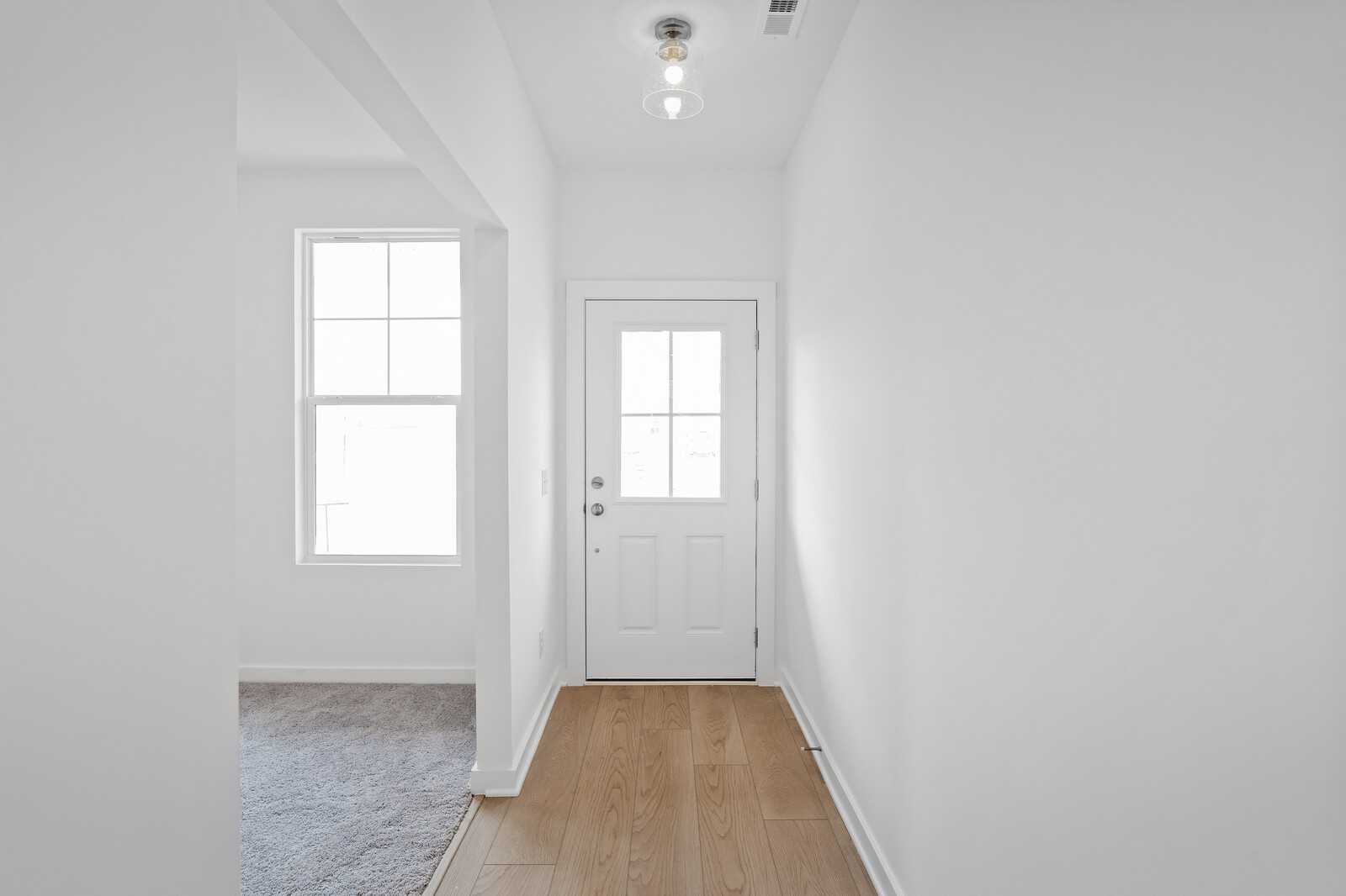 Bright hallway with oak hardwood floors, white glass-paneled door, and open archway in Davidson Homes The Logan B, Calista Farms, White House, TN