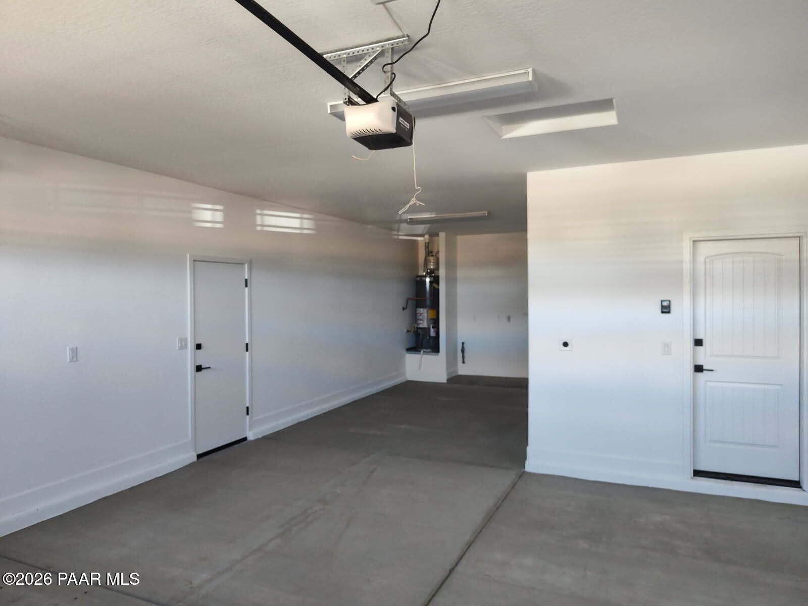 Spacious 3-car garage with overhead door opener, white walls, concrete floor, and utility closet in Davidson Homes The Harmony C, Prescott Valley, AZ