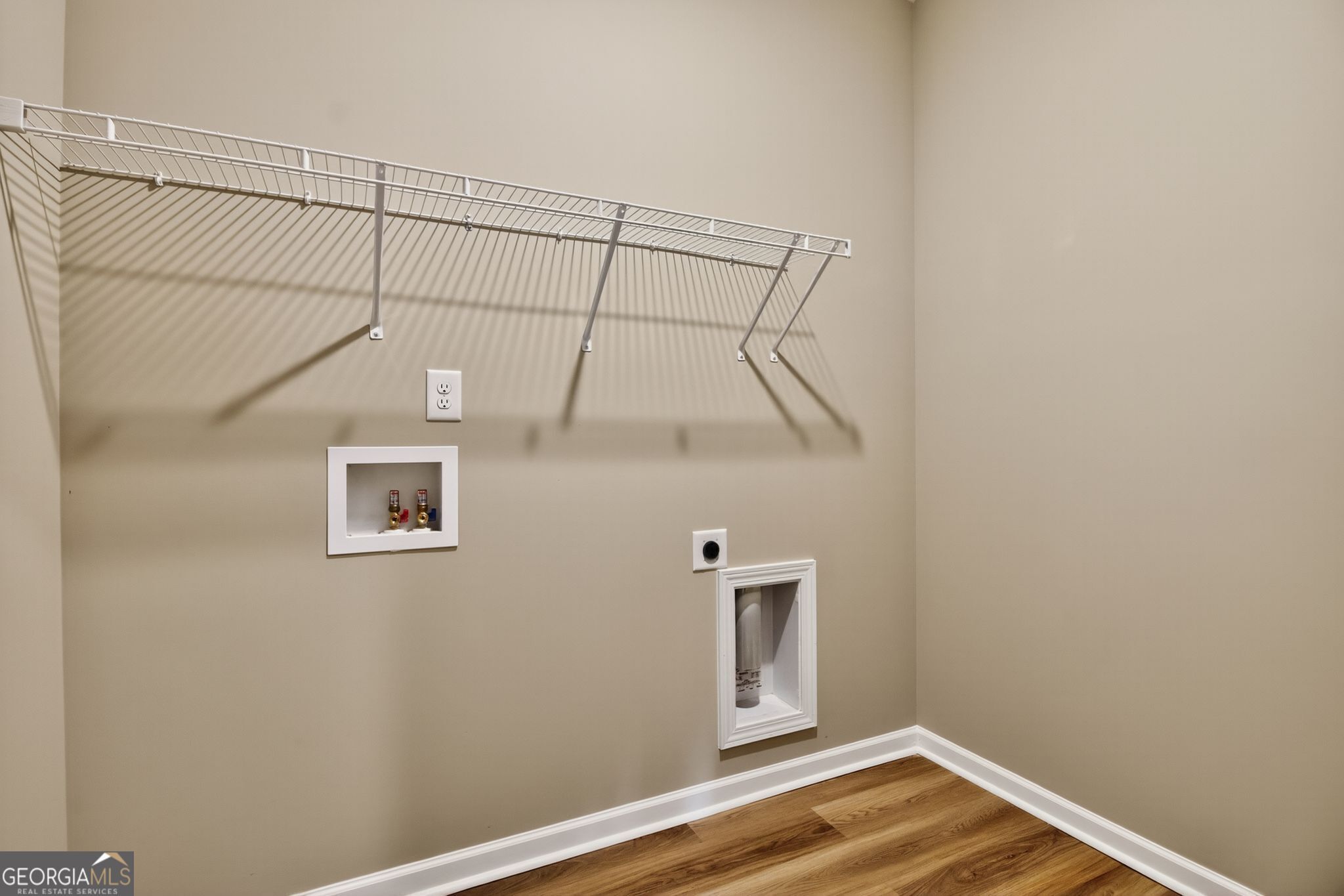 Functional laundry room with white wire shelving, outlets, and washer drain in The Luna 4-bedroom home, Ivy Glen, Perry, GA