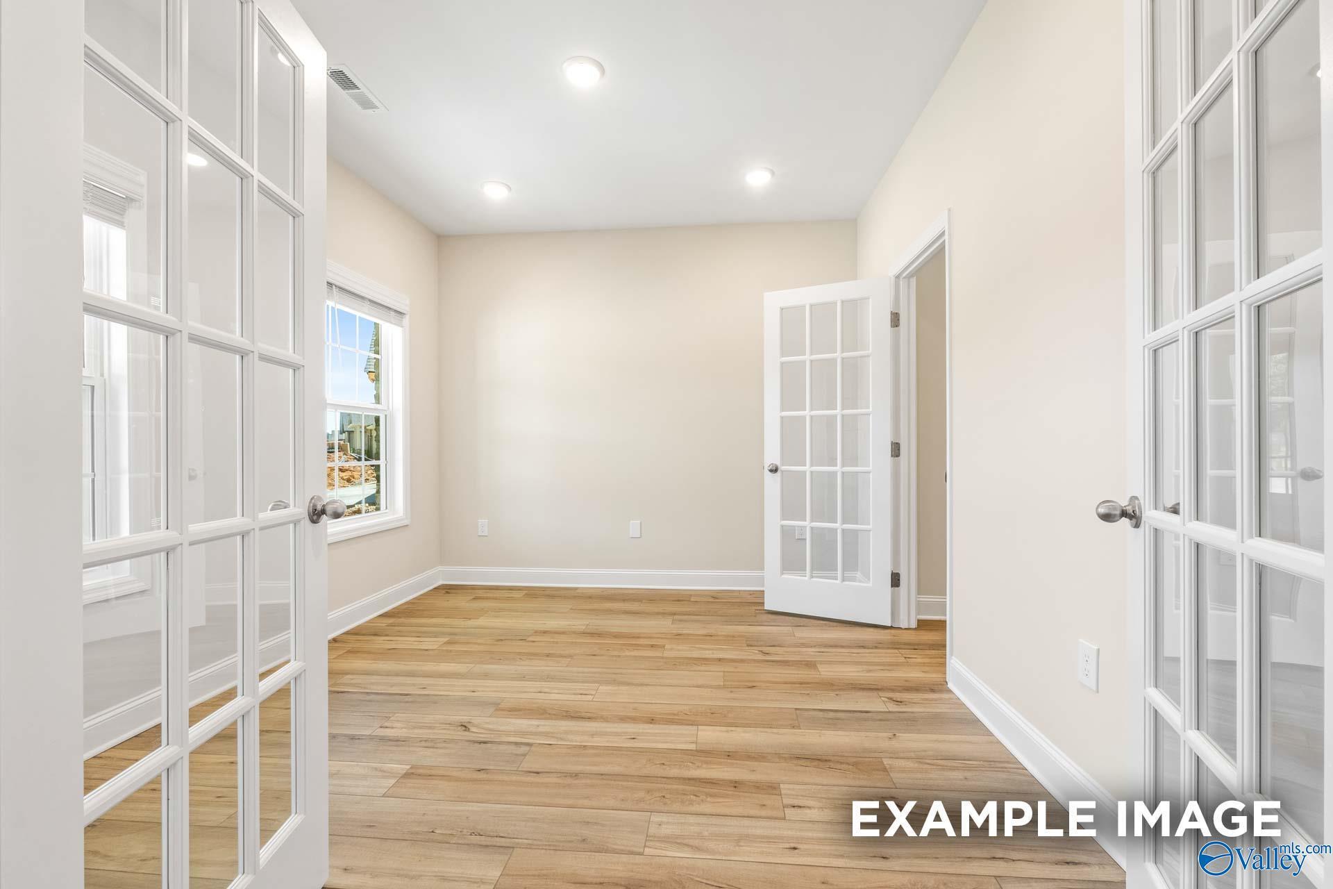 Bright empty room with beige walls, hardwood floors, French doors, and window in Davidson Homes The Shelby B, Arab, Alabama