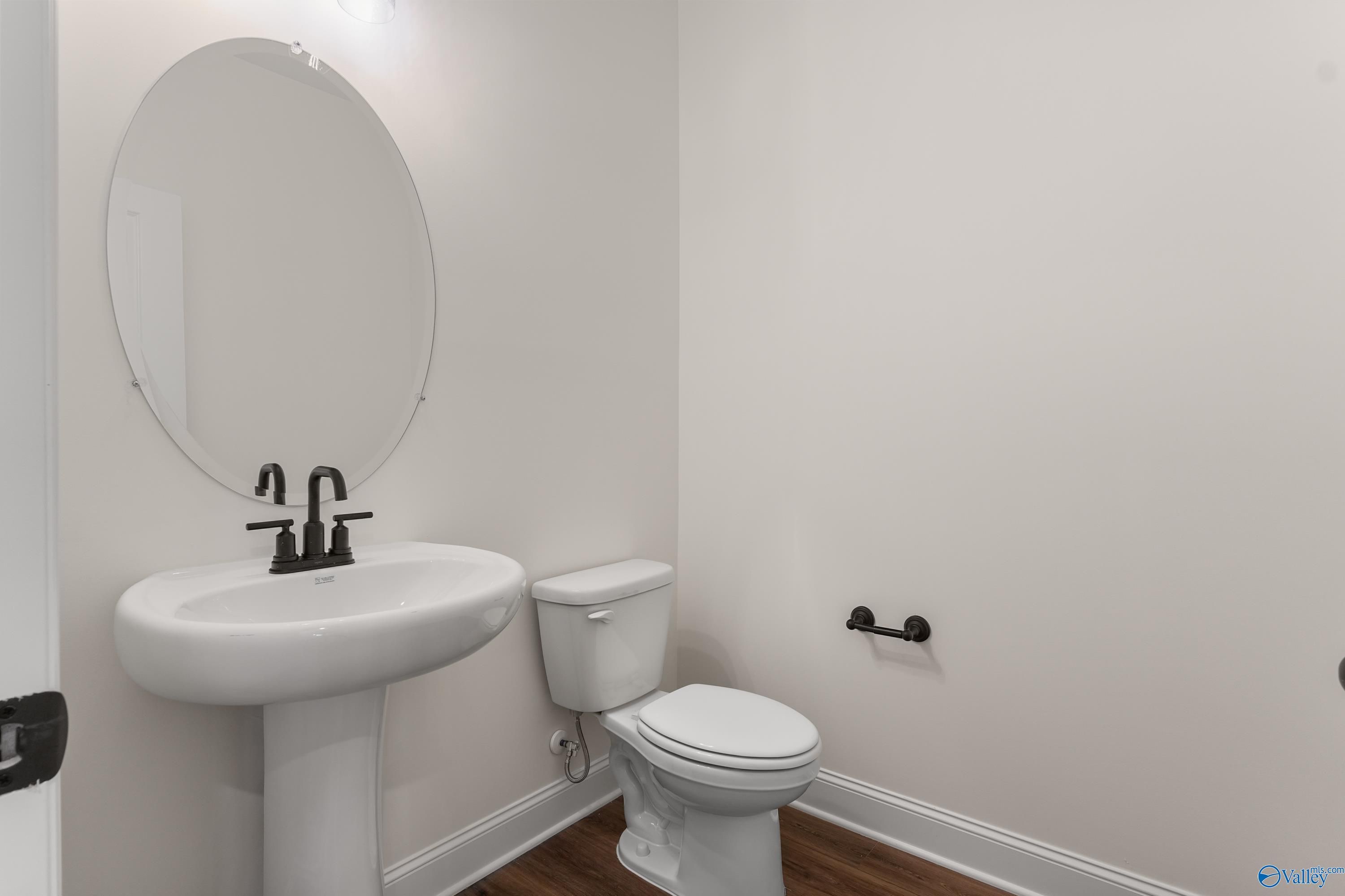 Modern powder room featuring pedestal sink, round mirror, toilet, and black fixtures in Davidson Homes The Finleigh, Harvest, Alabama