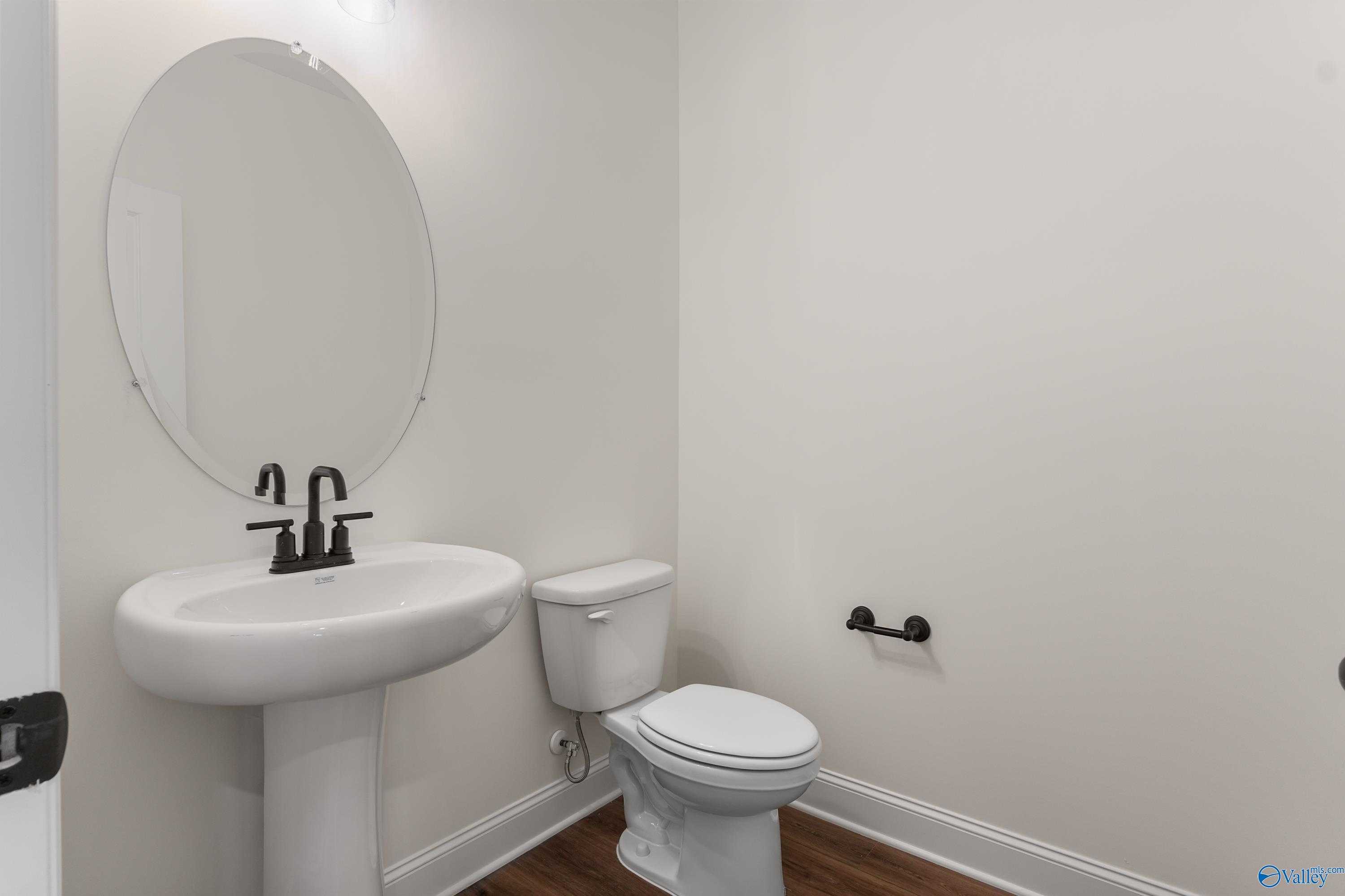 Modern powder room featuring pedestal sink, round mirror, toilet, and black fixtures in Davidson Homes The Finleigh, Harvest, Alabama