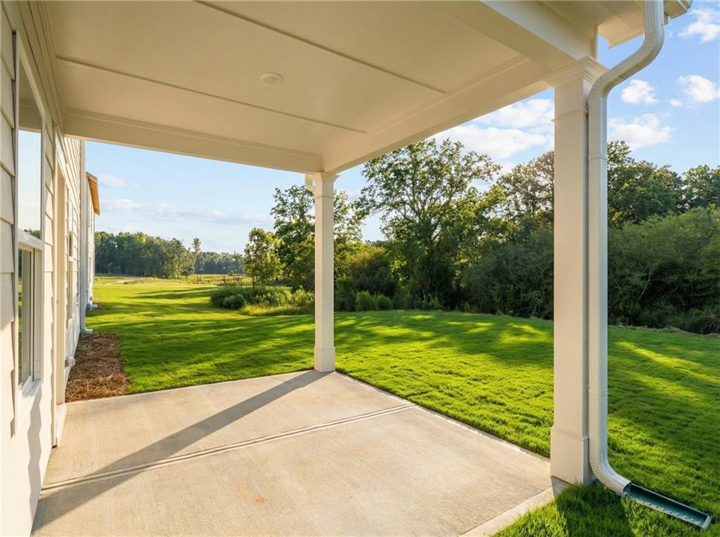 Covered back patio with white columns overlooking lush green lawn and woods in Davidson Homes The Rabun C, The Bluffs, Canton, Georgia