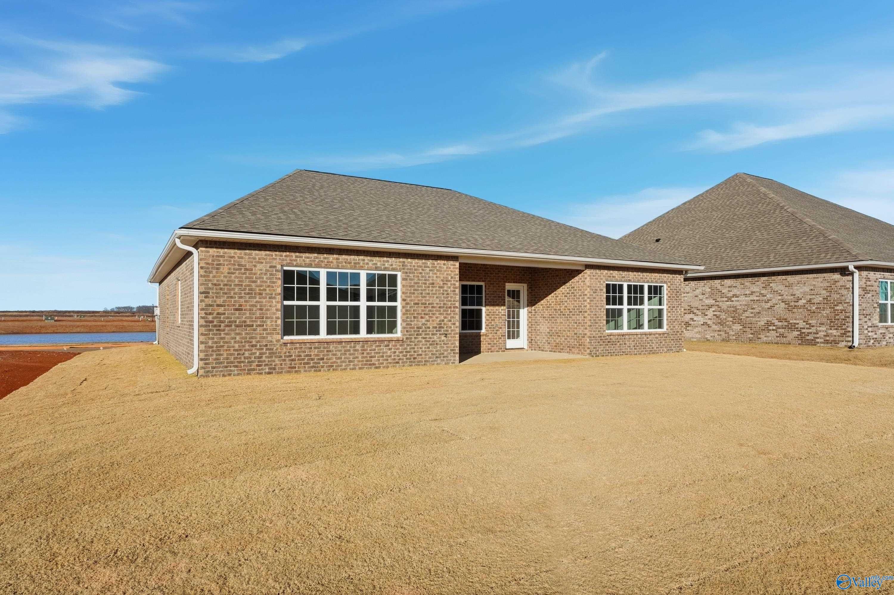 Single-story brick home exterior with gabled roof, large windows, and covered entry on grassy lot in Kendall Downs, Toney, Alabama