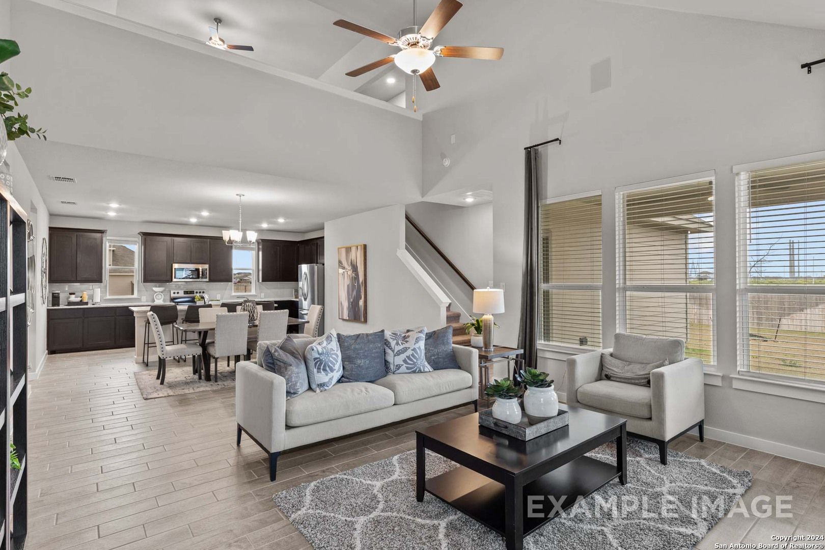 Open-concept great room with modern kitchen, dining table, gray sofa, and large windows in Davidson Homes The Collin A, Seguin, Texas