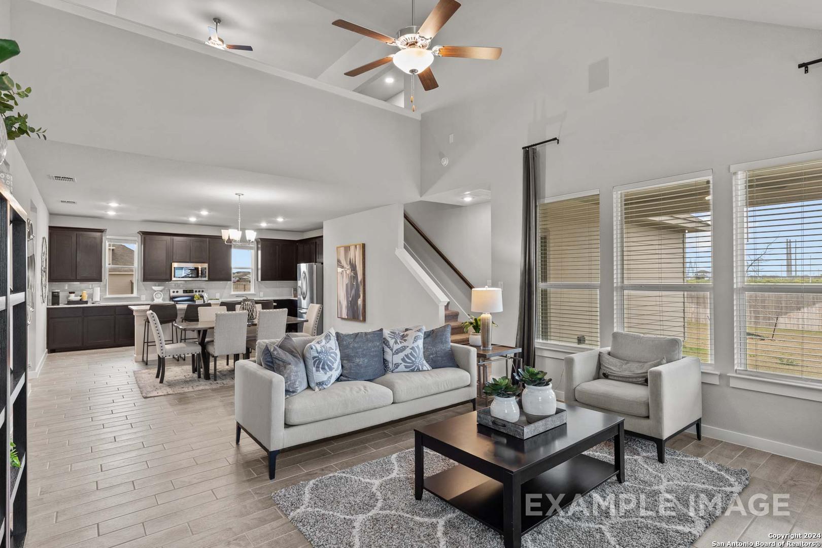 Open-concept great room with modern kitchen, dining table, gray sofa, and large windows in Davidson Homes The Collin A, Seguin, Texas